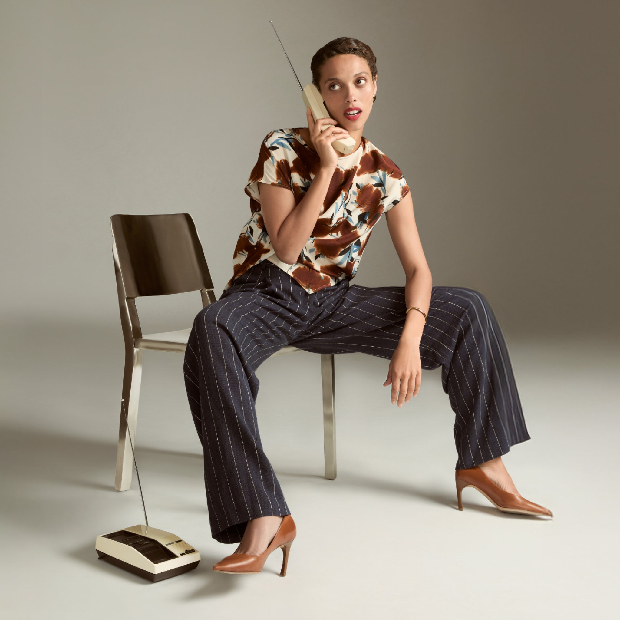Woman sitting on a chair holding a vintage phone with a plain background