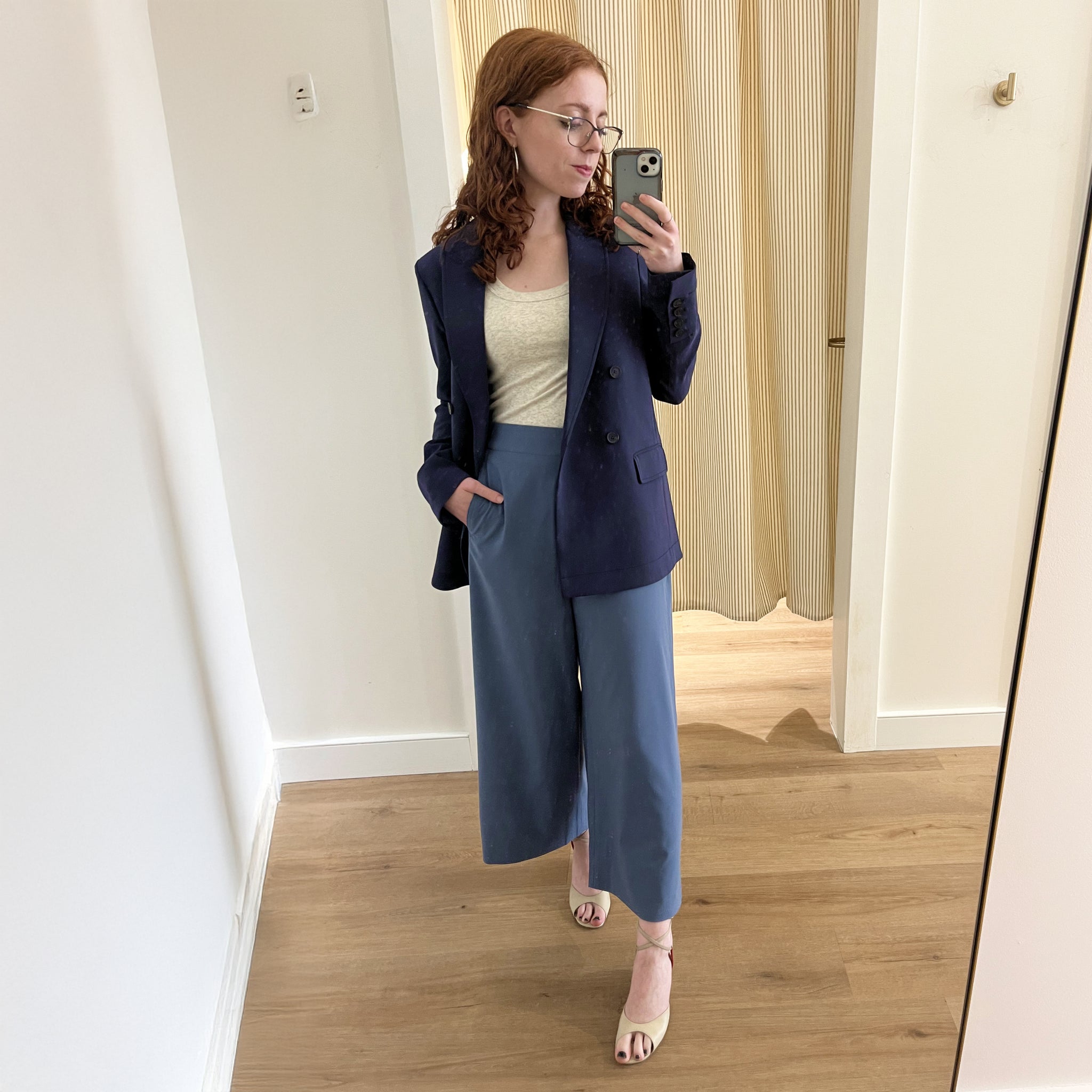 Woman taking a mirror selfie wearing a navy blazer and blue pants indoors.