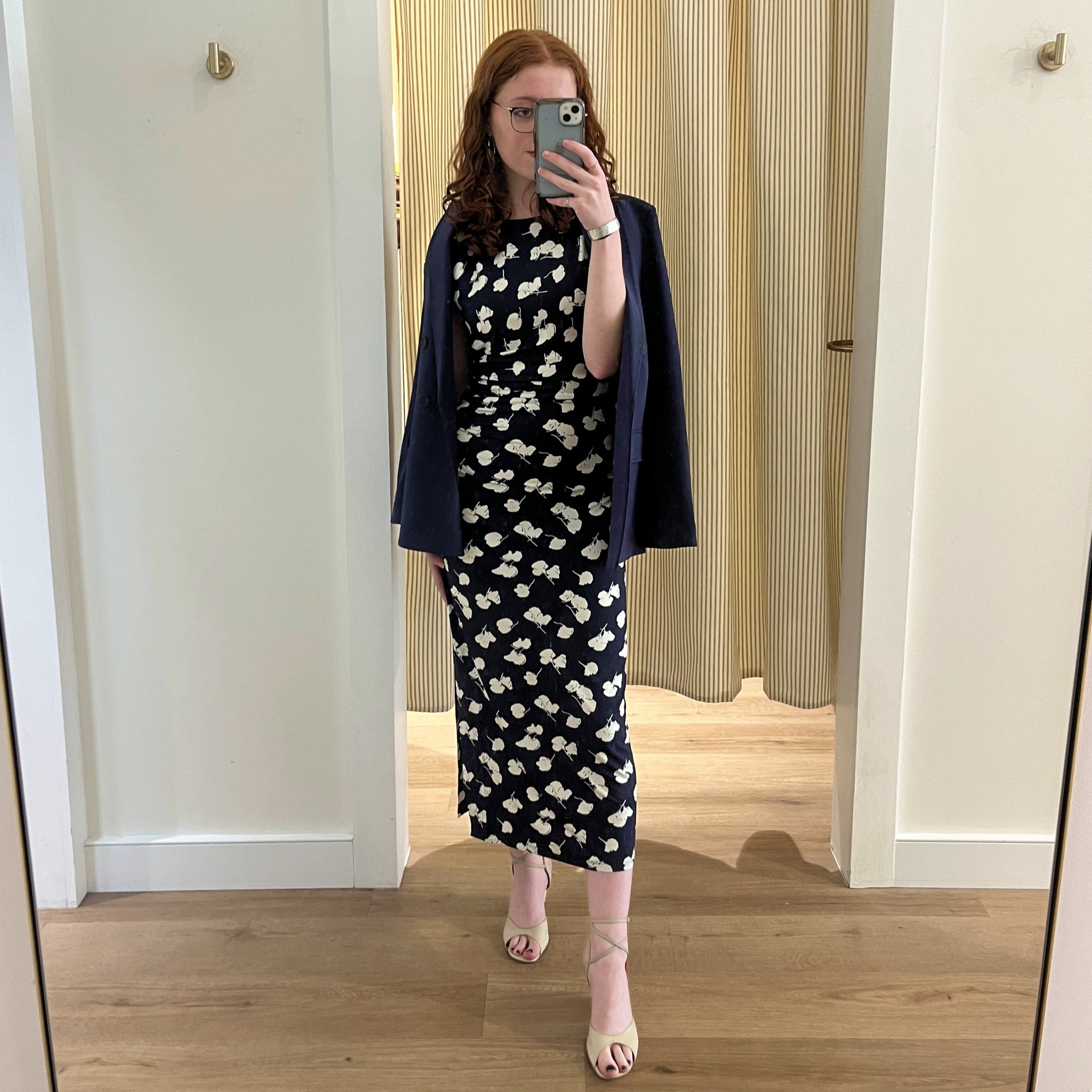 Woman taking a mirror selfie wearing a navy dress with white floral pattern and navy cardigan.
