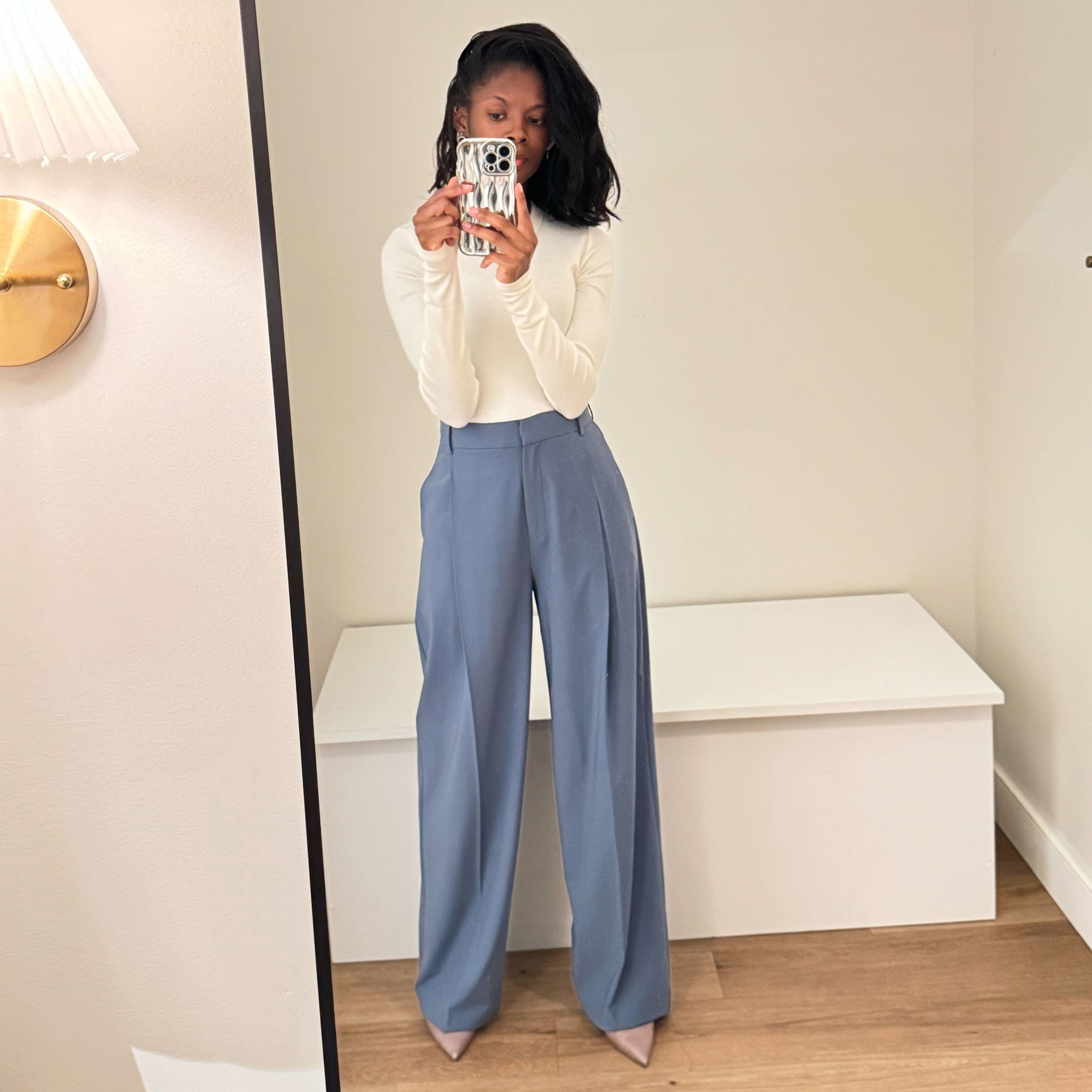 Person wearing a white sweater and blue pants taking a mirror selfie.