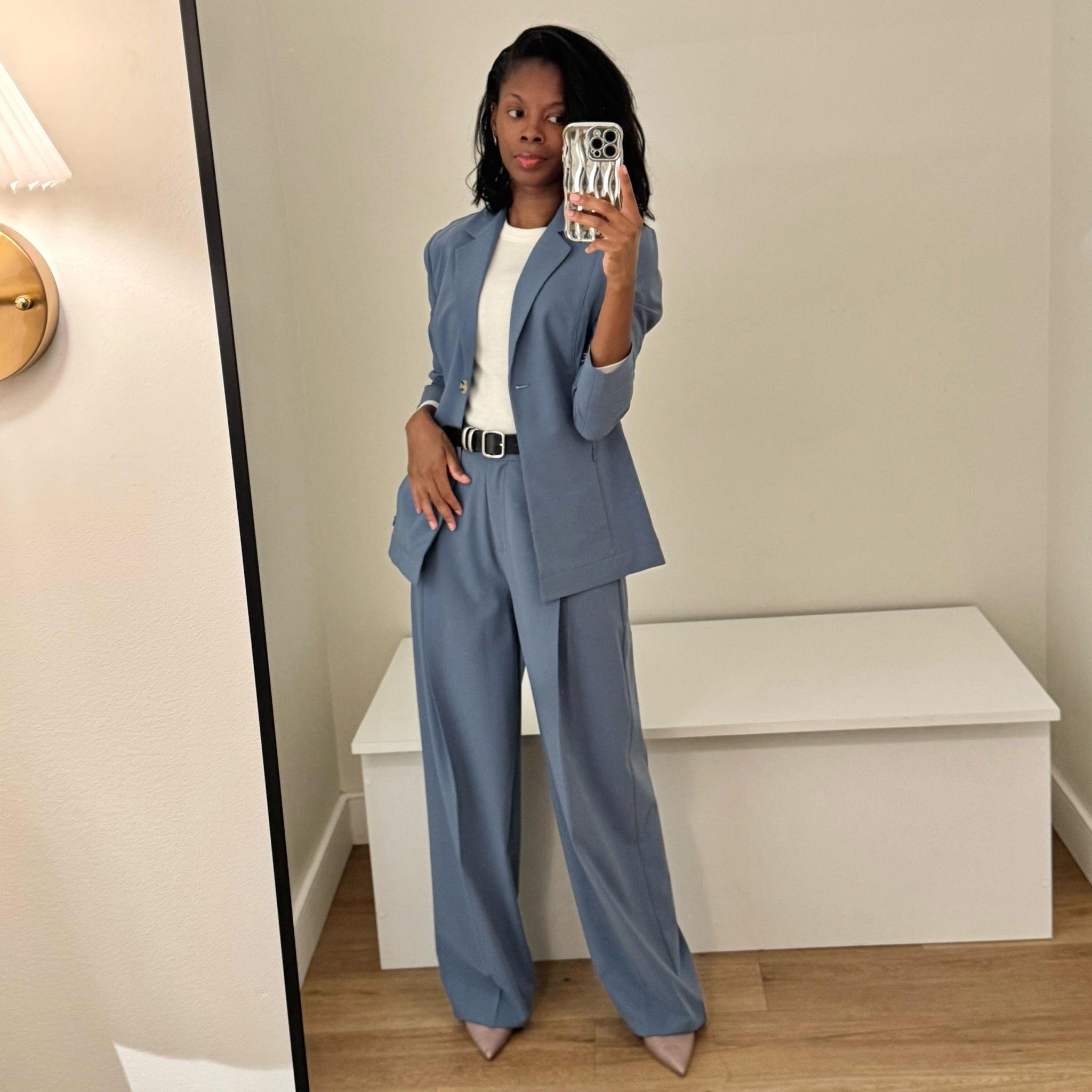 Person wearing a blue suit taking a mirror selfie in a room with a white bench.