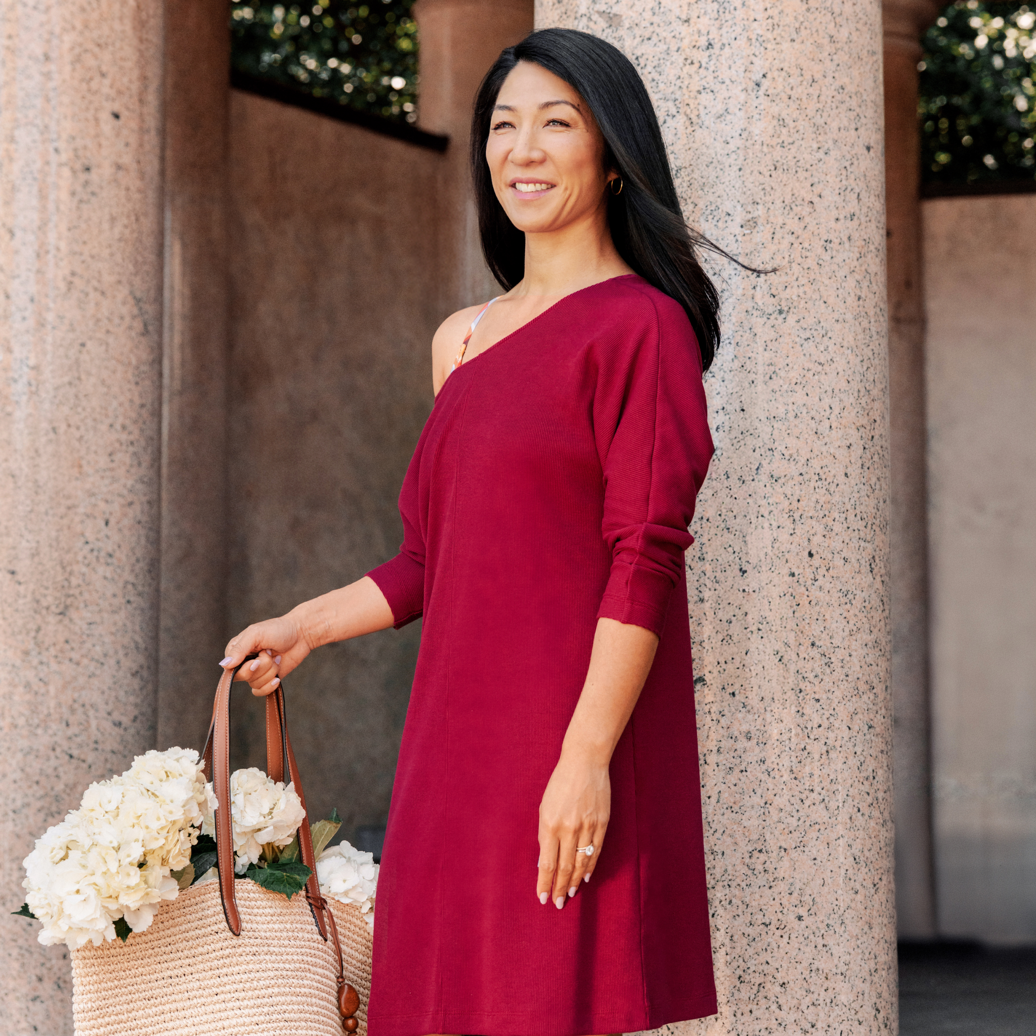 Woman in a red dress holding flowers, standing against a stone wall