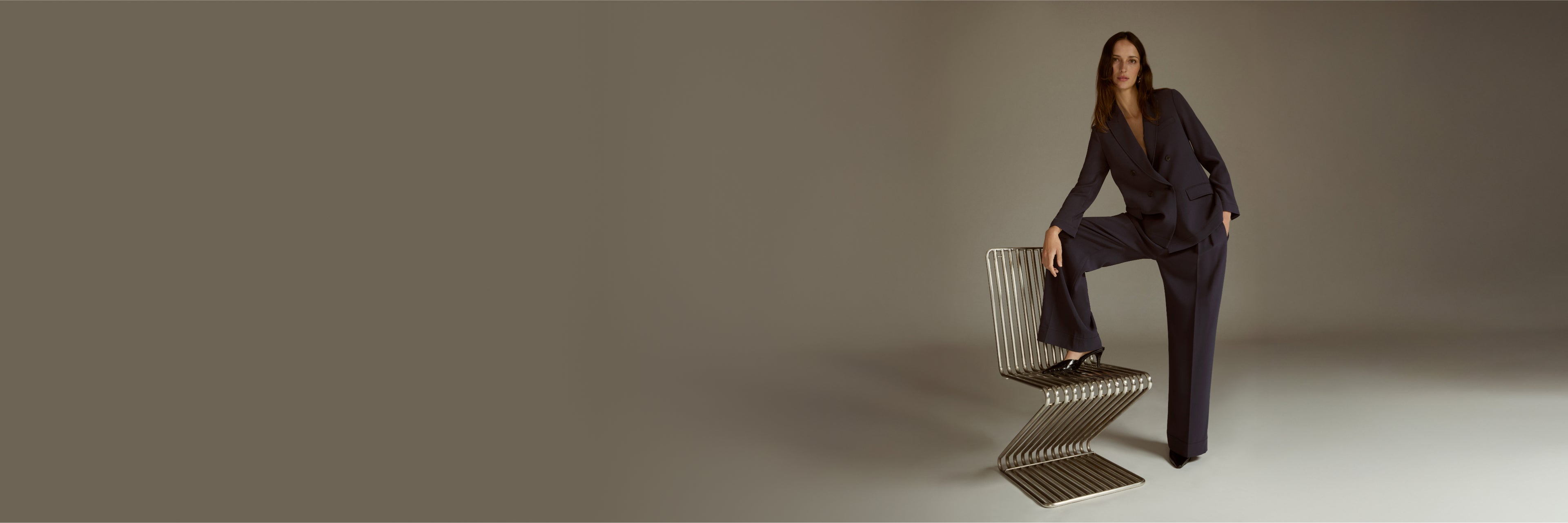 Woman in a dark suit sitting on a chair against a plain background