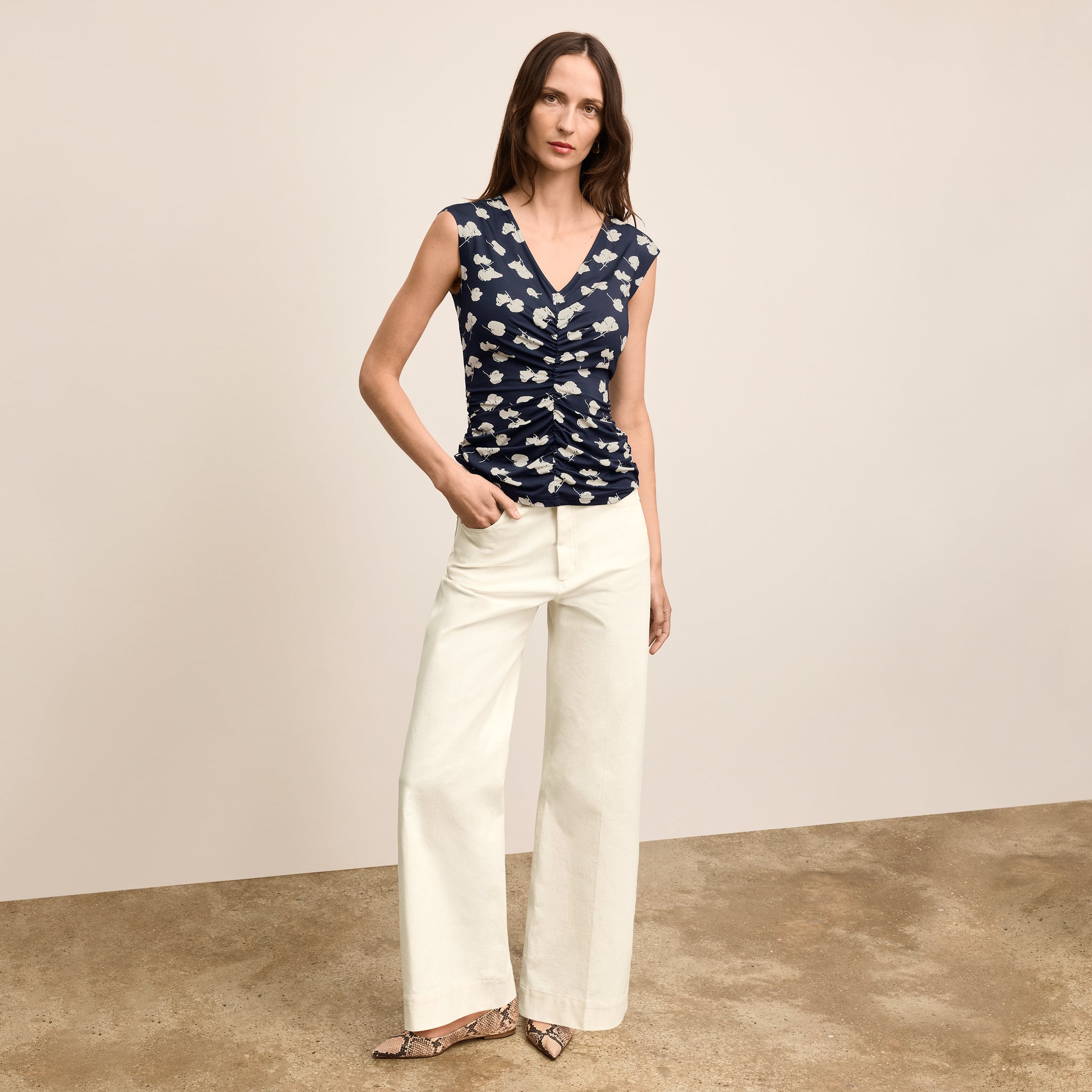 Woman wearing a navy floral top and white pants on a beige background