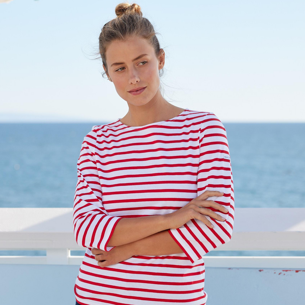 Woman wearing a red and white striped shirt standing by a railing with a clear blue sky and ocean in the background.