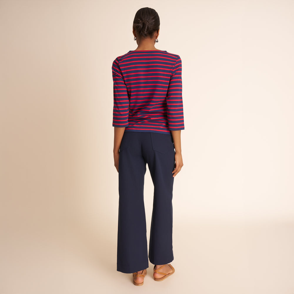 Woman wearing a red and blue striped top and navy pants on a beige background