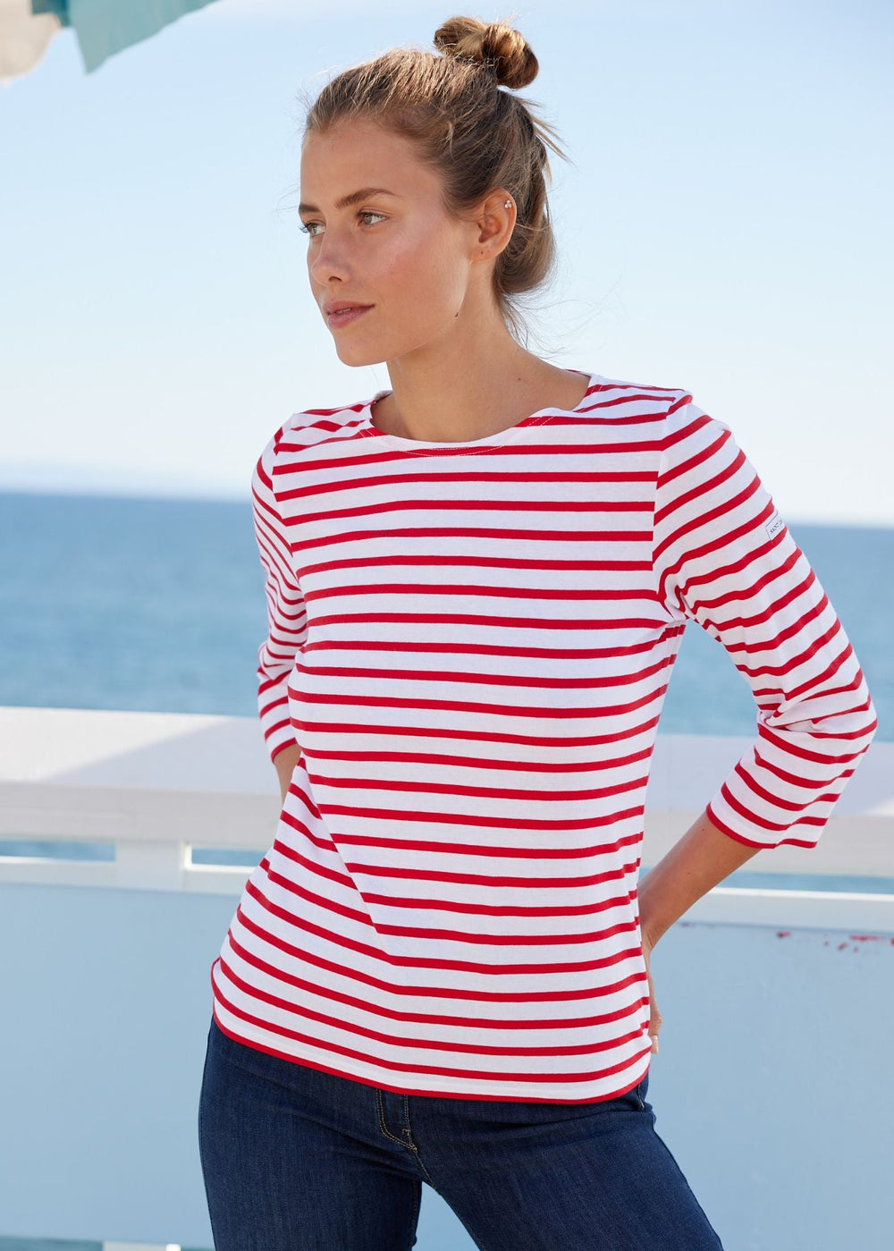 Woman wearing a red and white striped shirt with blue jeans by the sea.