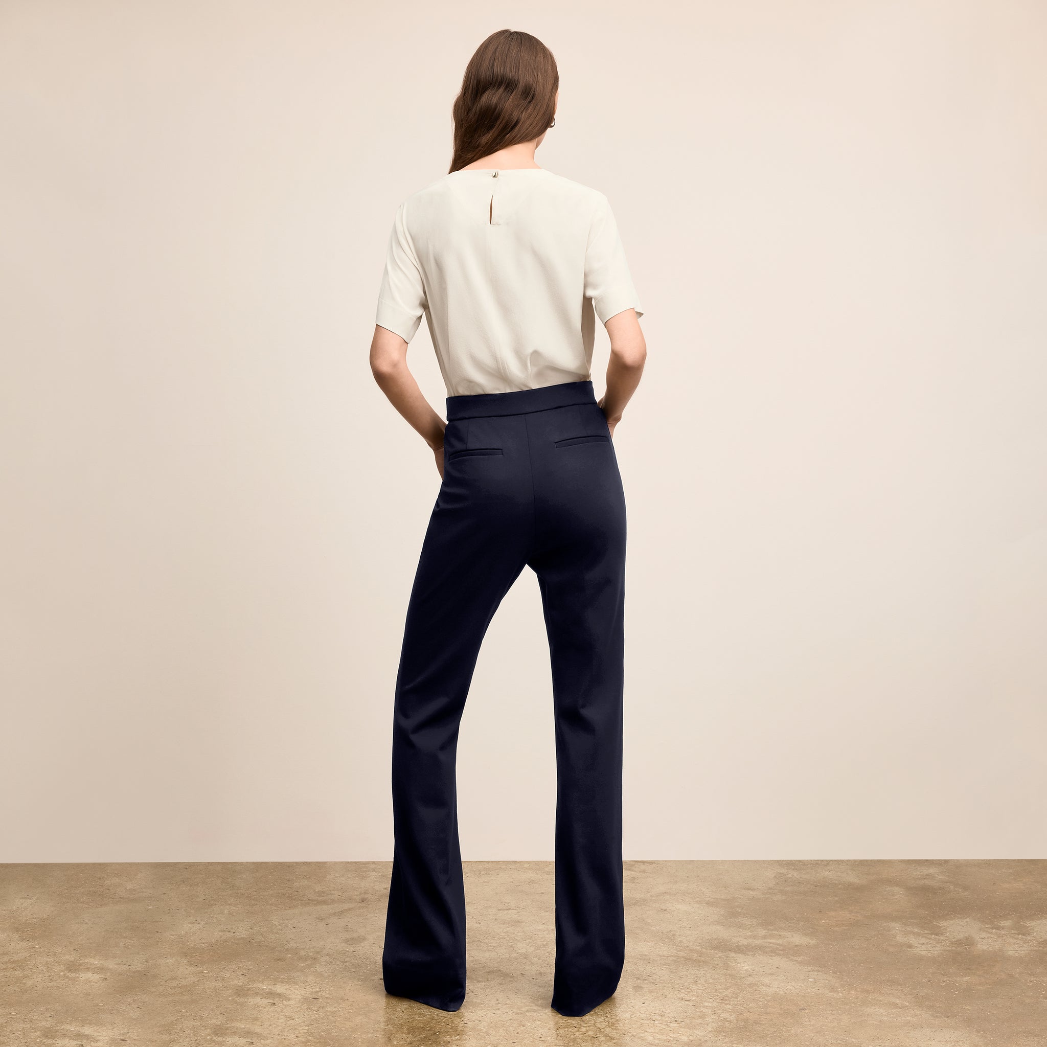 Person wearing a white shirt and navy pants standing against a beige wall.