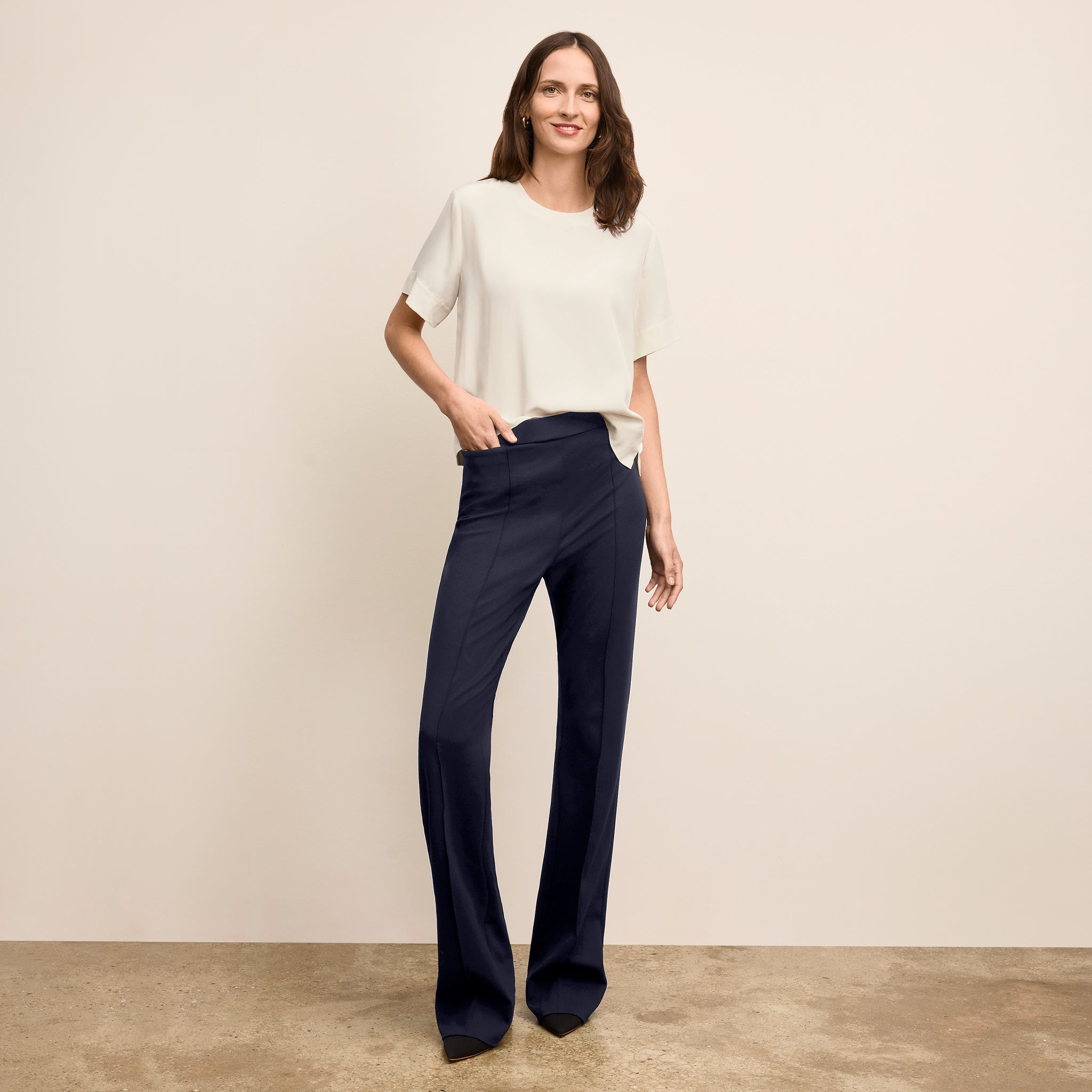 Woman wearing a white top and navy pants against a beige background