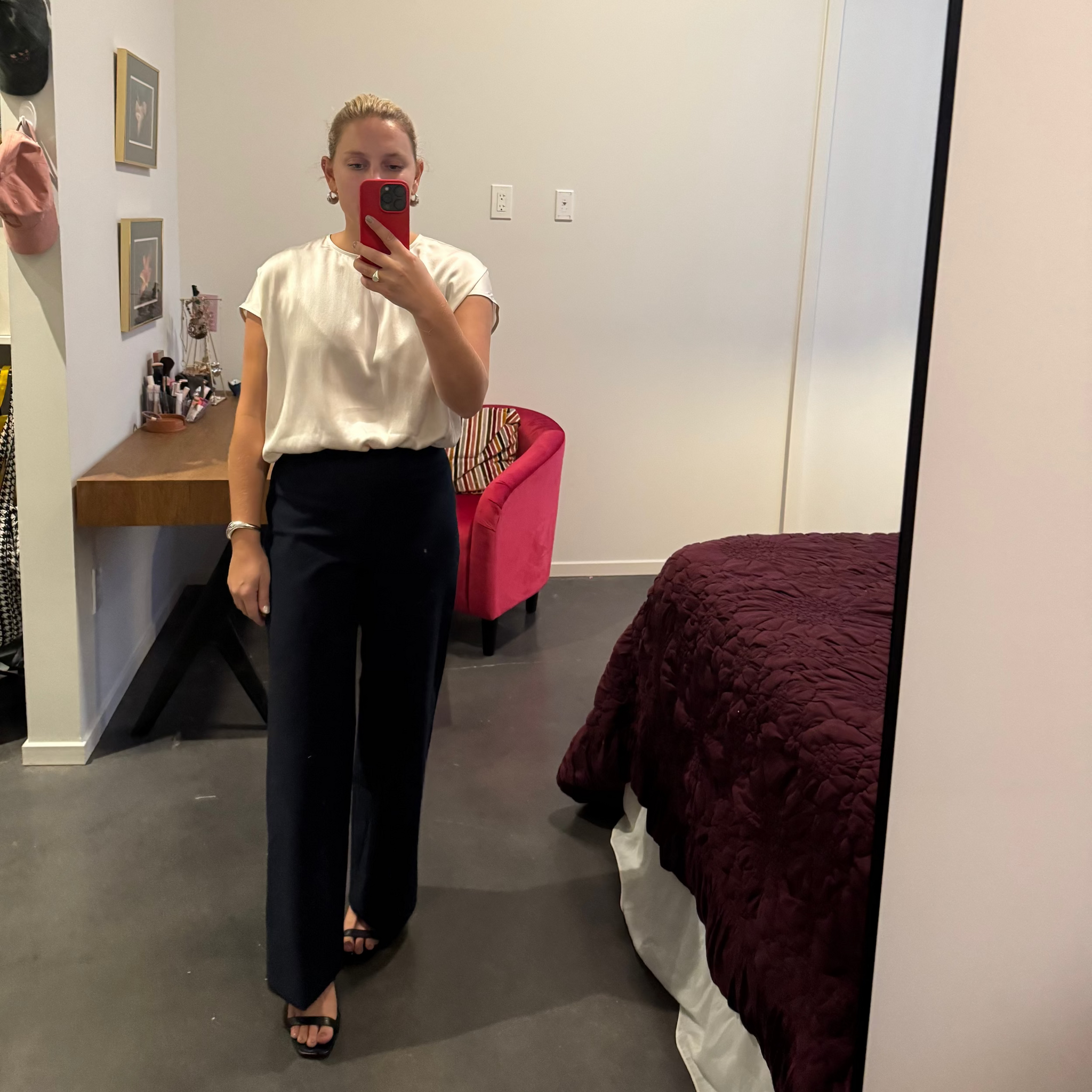 Person taking a mirror selfie in a room with a bed and furniture.