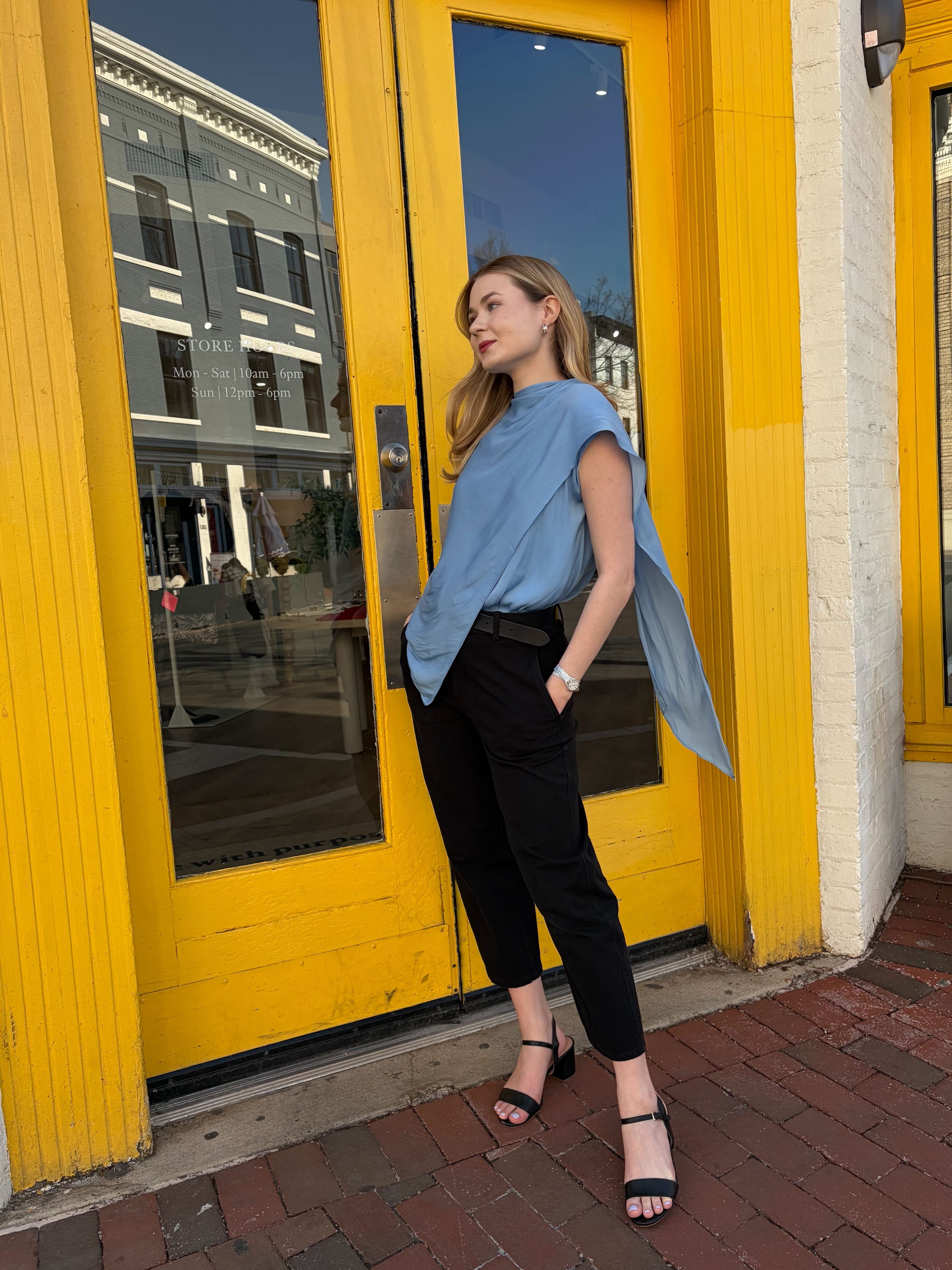 Woman in a blue shirt and black pants standing in front of a yellow door.
