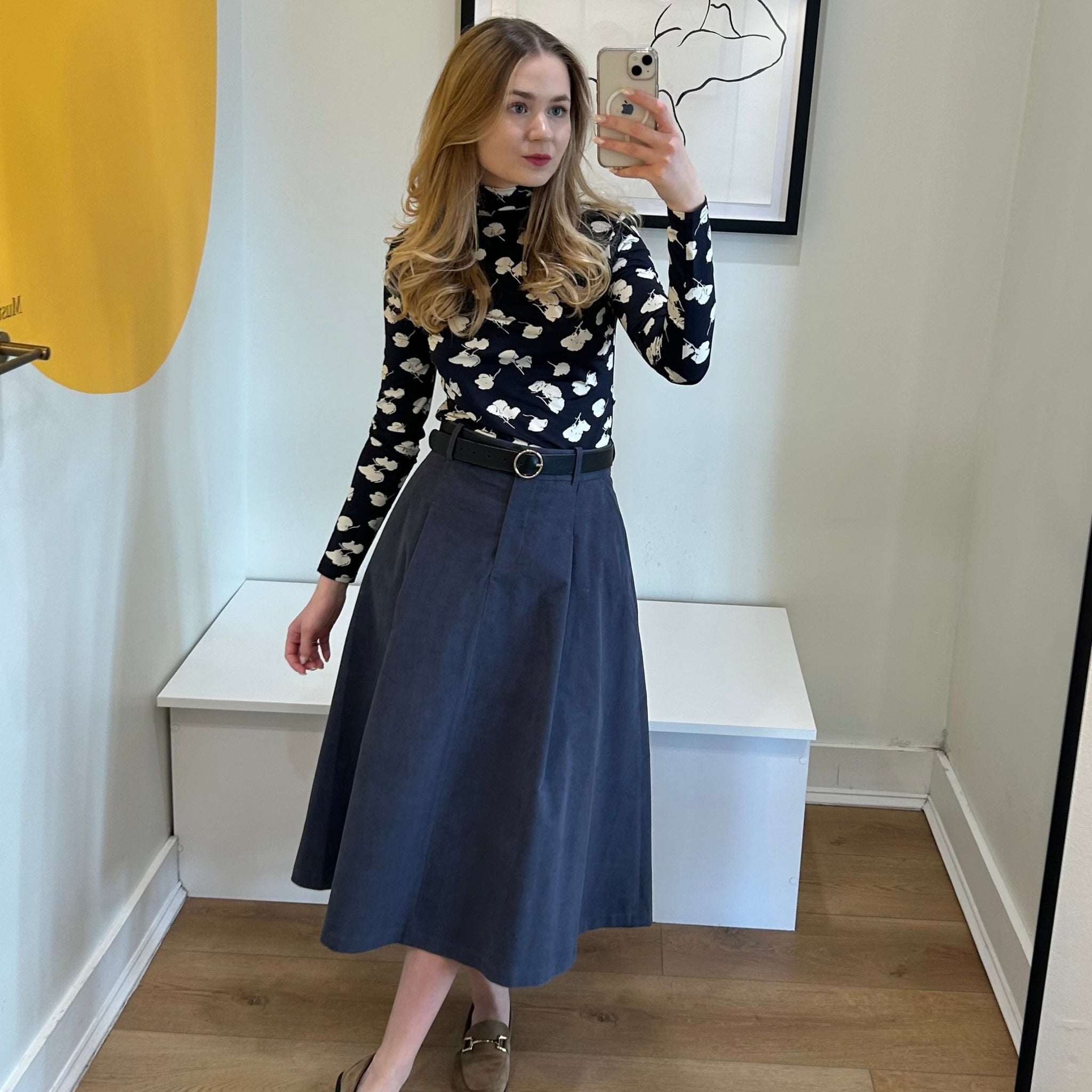 Woman taking a mirror selfie wearing a blue and white patterned top and blue skirt.