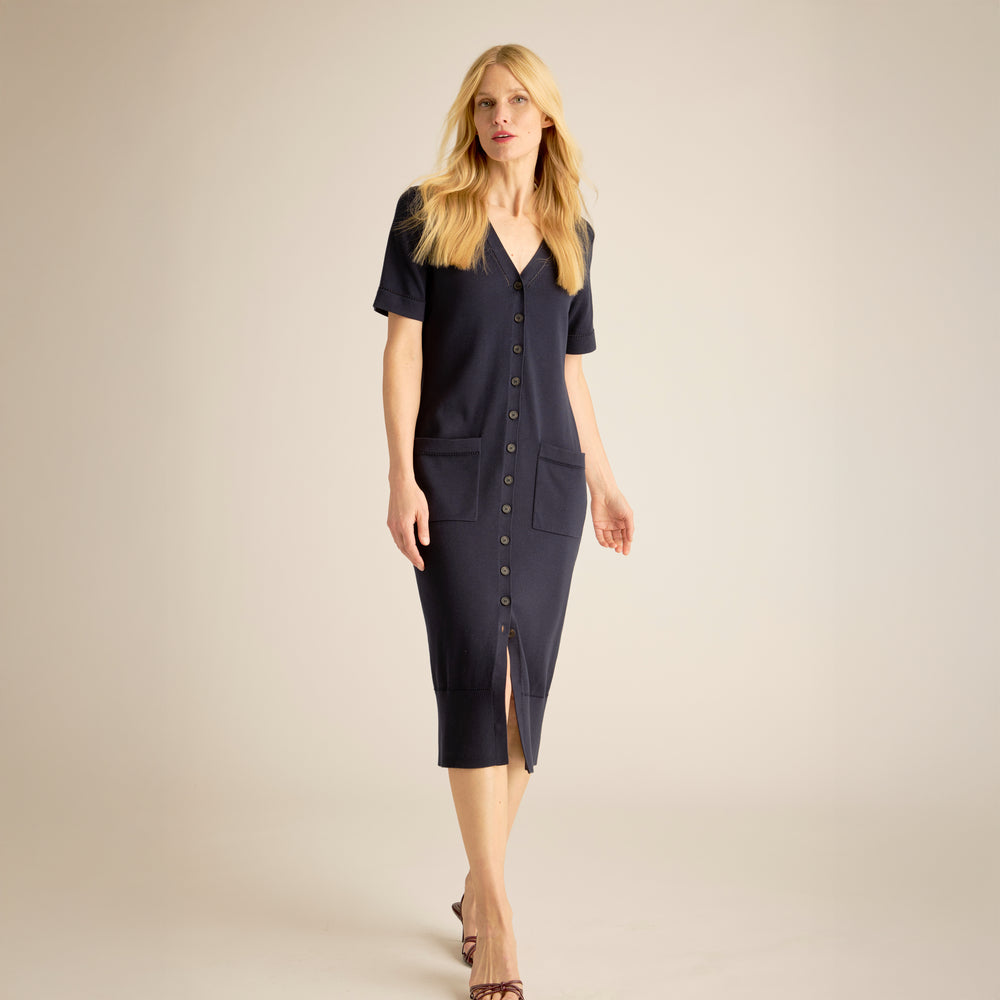 Woman wearing a navy blue dress with a V-neckline and short sleeves on a beige background