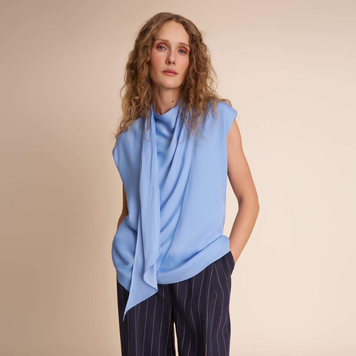 Woman wearing a light blue sleeveless top against a beige background