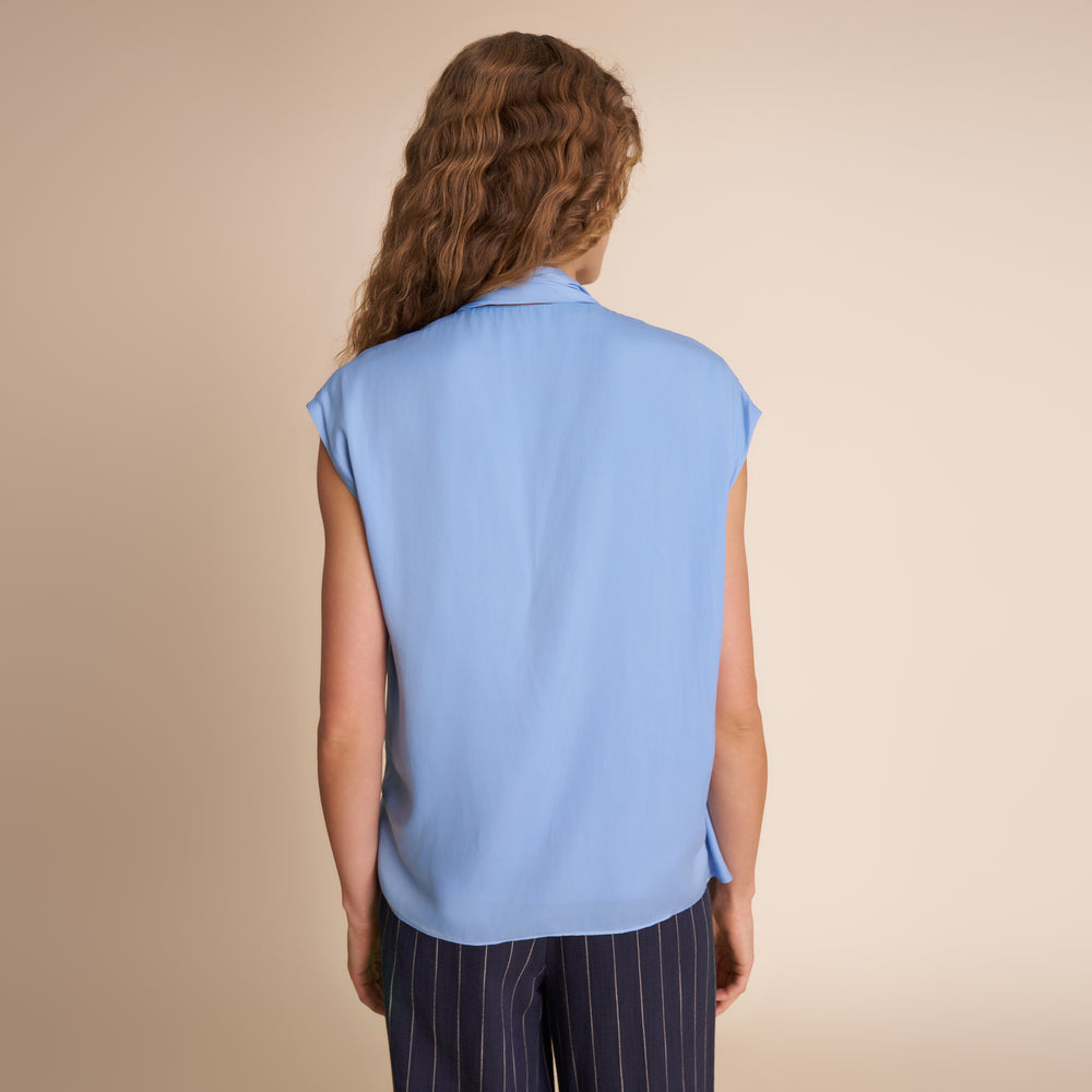 Person wearing a light blue sleeveless top with dark pants on a beige background