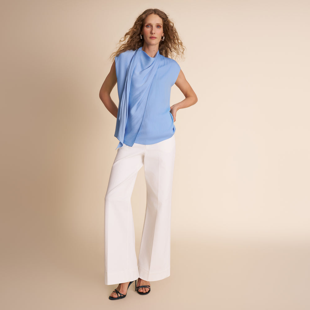 Woman wearing a light blue sleeveless top and white pants on a beige background