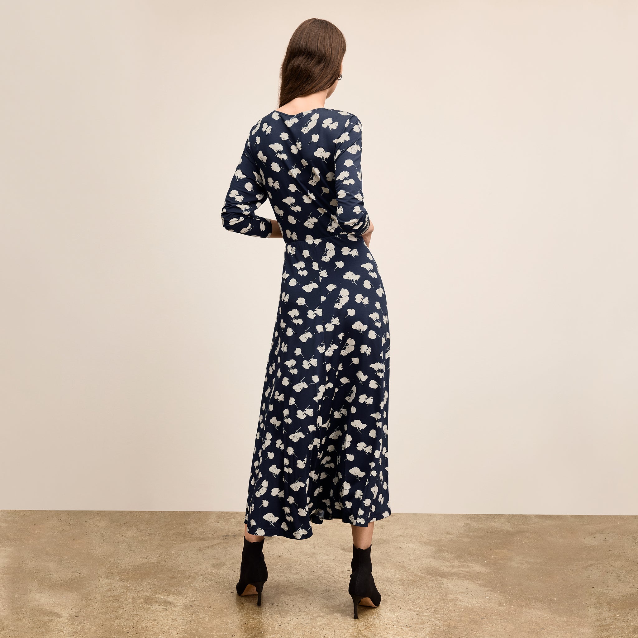 Woman wearing a navy dress with white floral pattern against a beige background