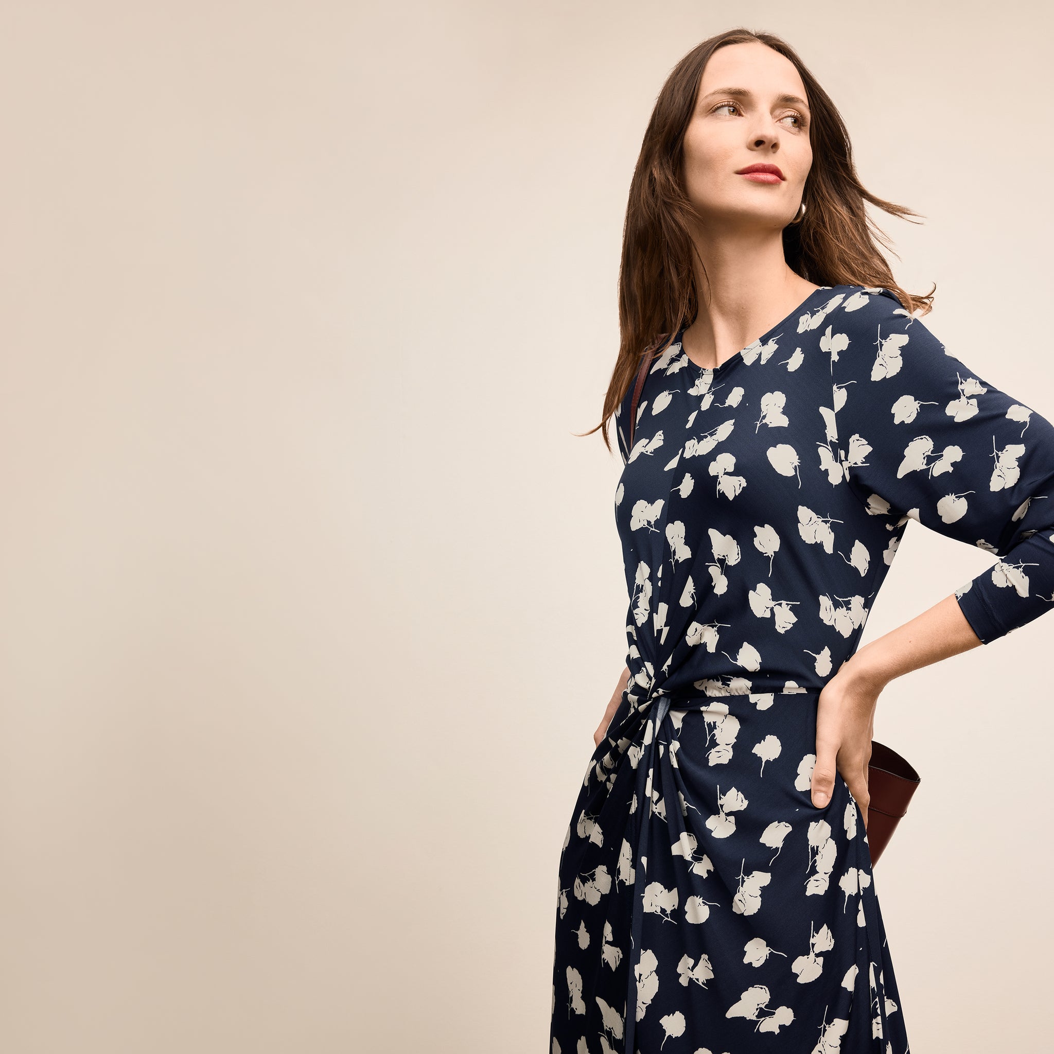 Woman wearing a navy dress with white floral pattern on a beige background