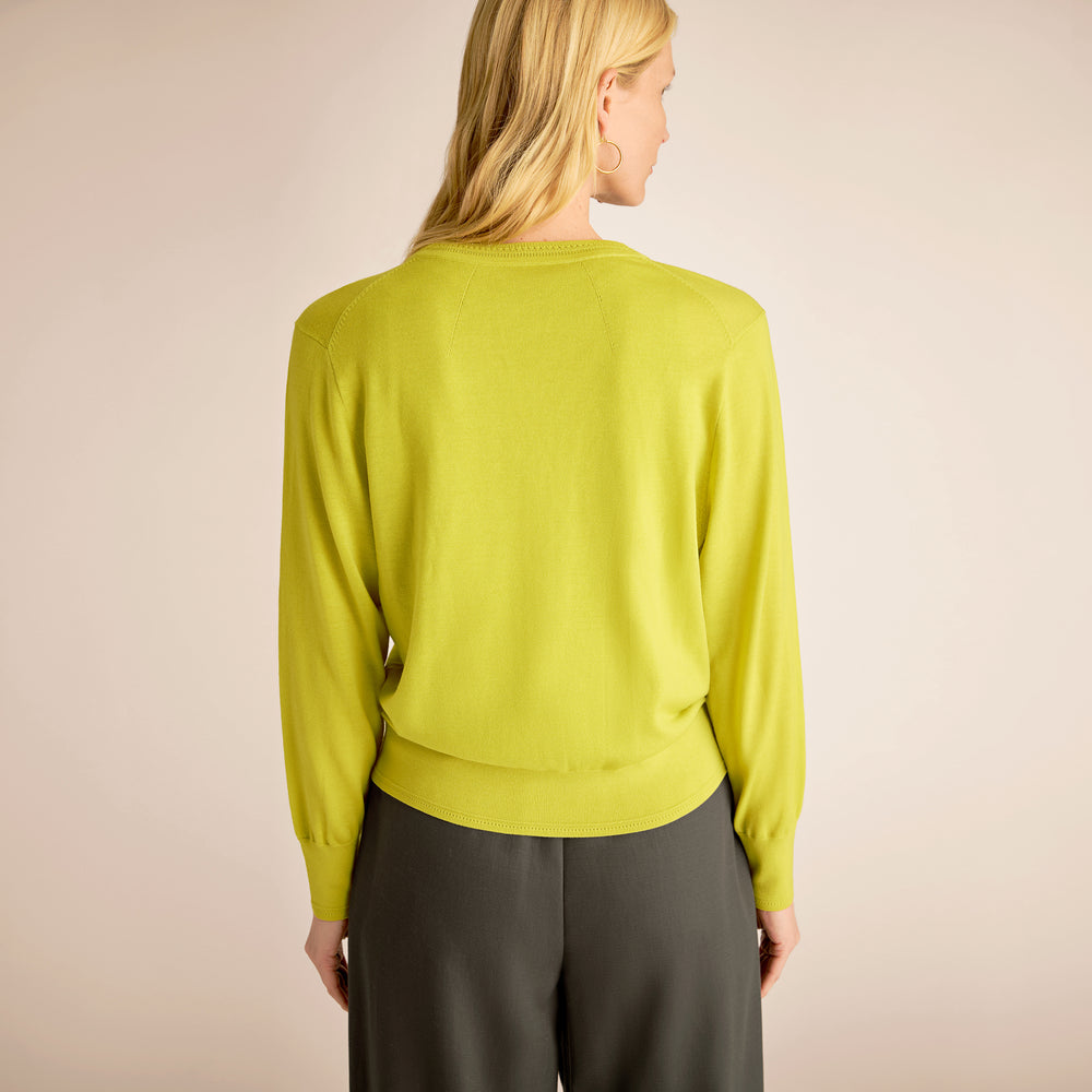 Person wearing a bright green sweater and gray pants on a beige background