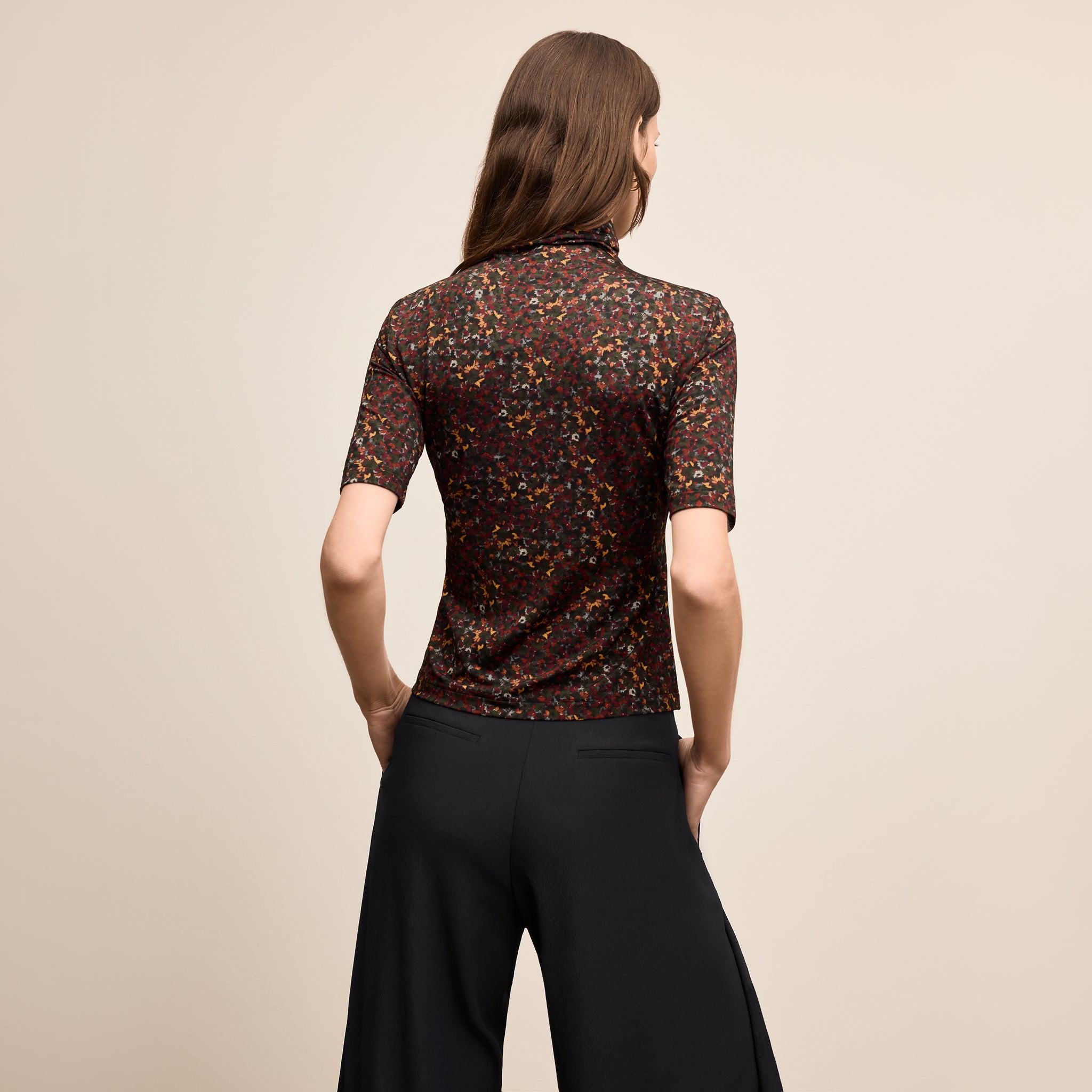 Woman wearing a patterned top and black pants on a beige background