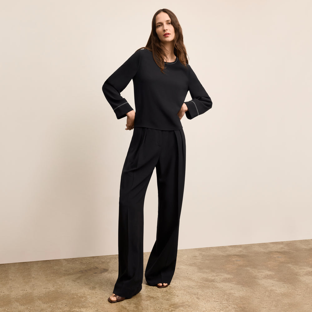 Woman wearing a black outfit standing against a beige wall.
