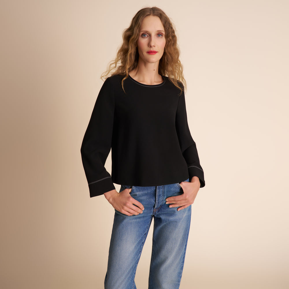 Woman wearing a black sweater and blue jeans against a beige background