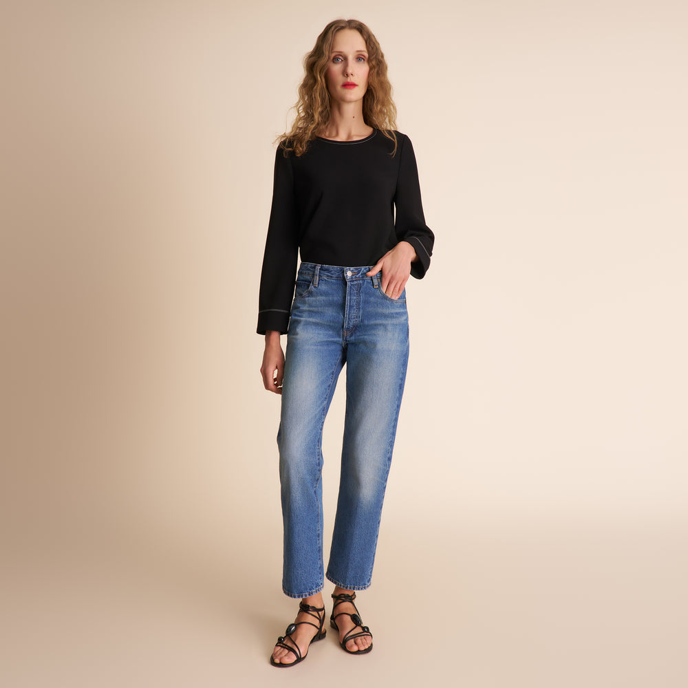 Woman wearing a black top and blue jeans on a beige background