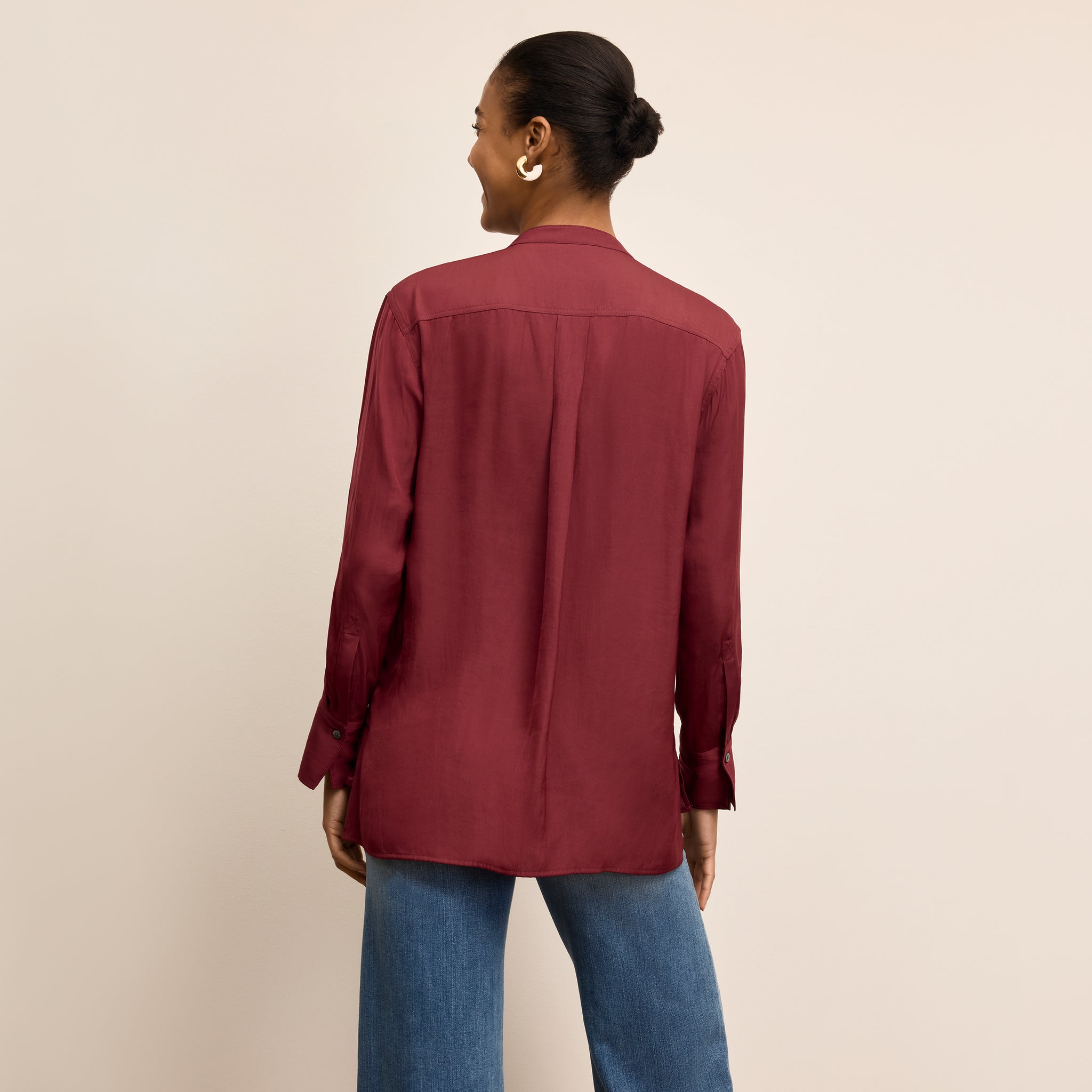Person wearing a burgundy shirt and blue jeans on a beige background