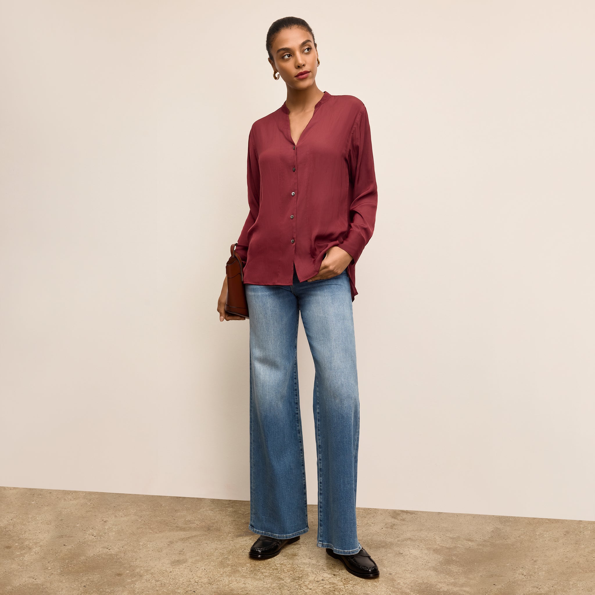 Woman wearing a burgundy blouse and blue jeans against a beige background