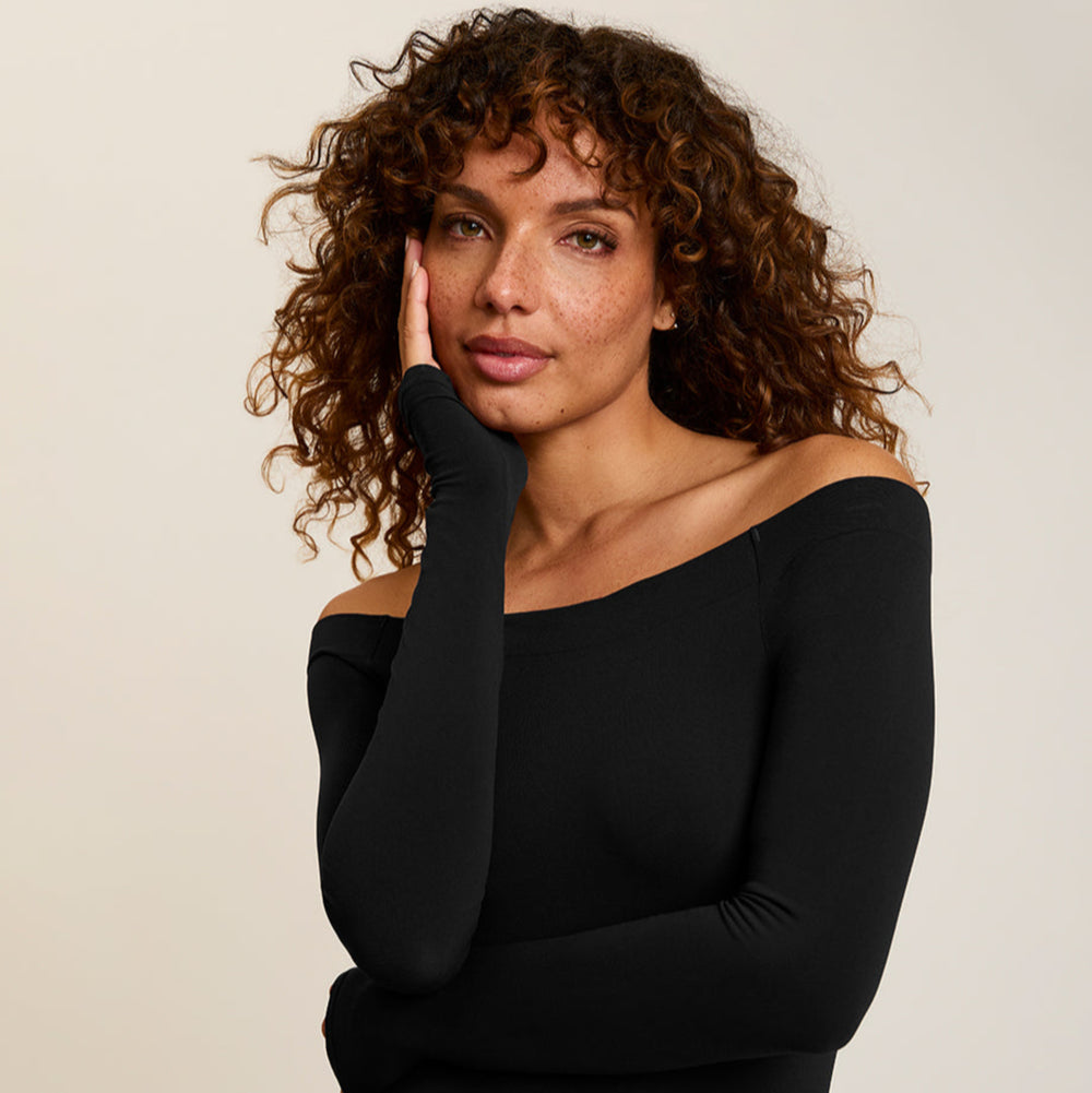 Woman wearing a black off-shoulder top against a beige background