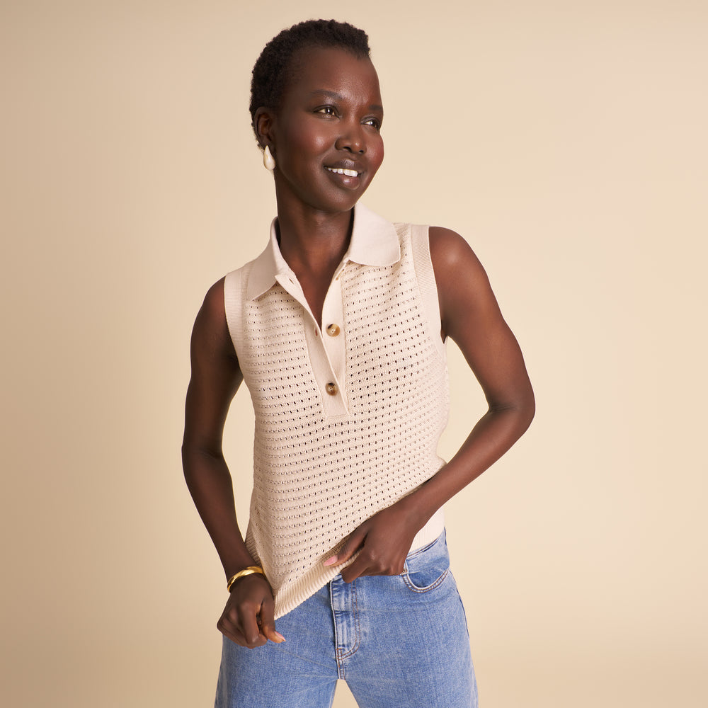 Woman wearing a beige sleeveless top with buttons and blue jeans on a beige background