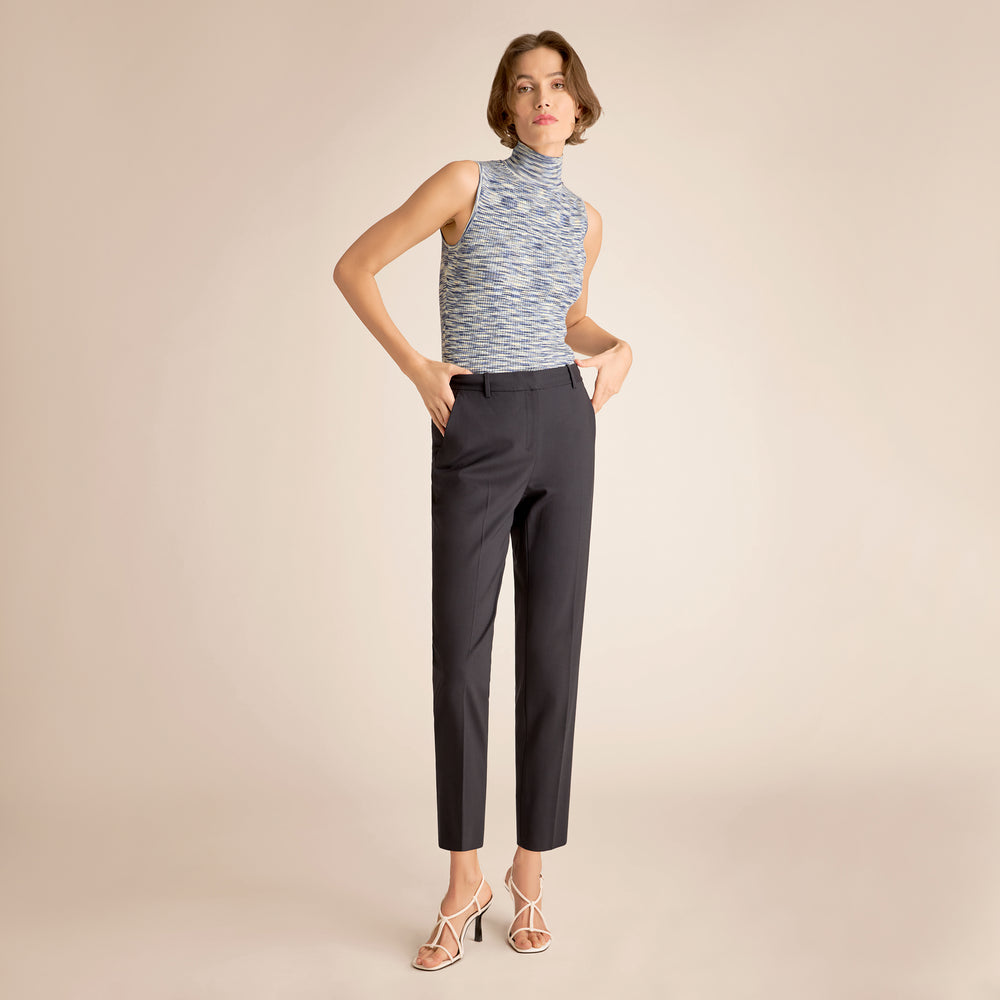 Woman wearing a sleeveless patterned top and dark pants on a beige background