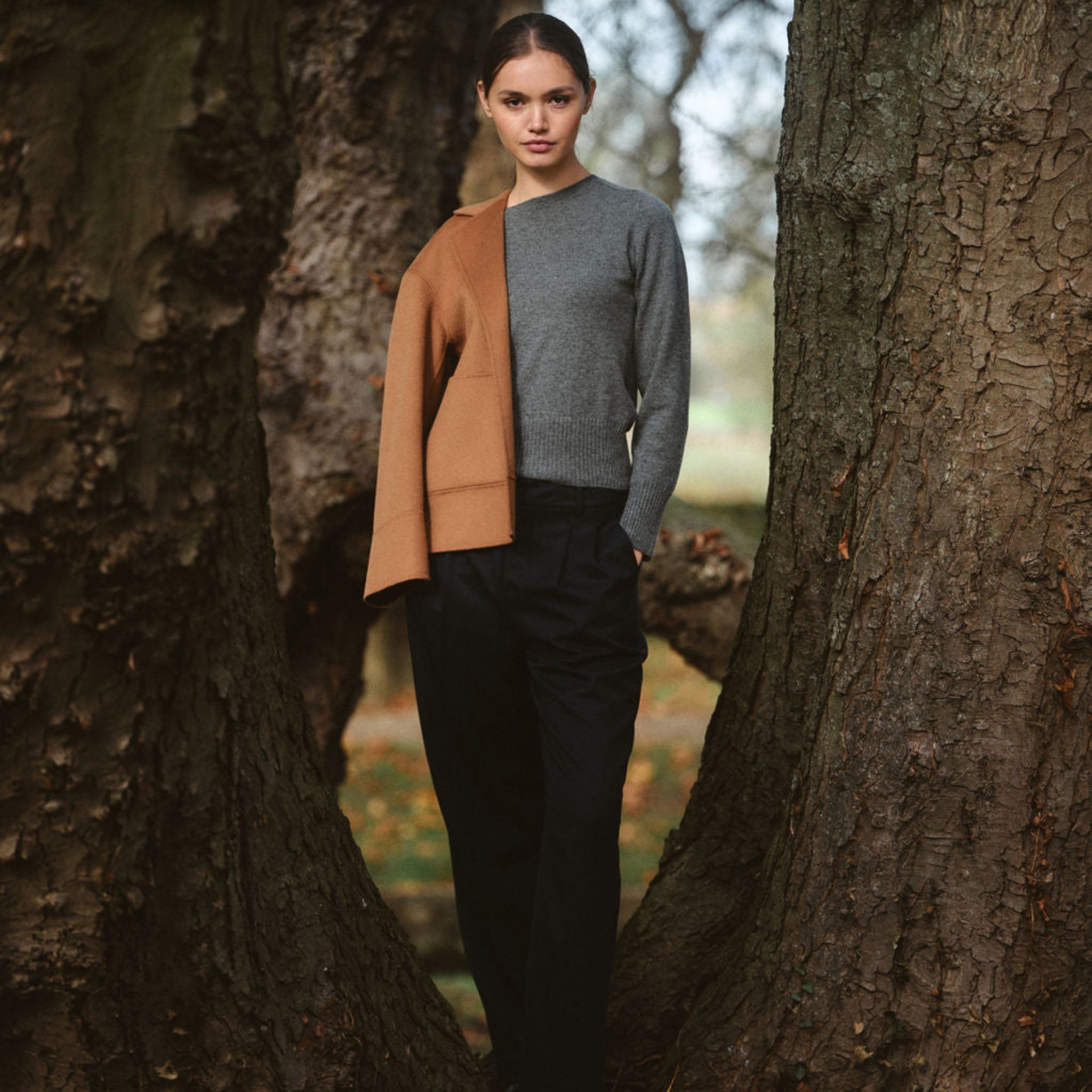 Woman standing between two large trees in a forest setting
