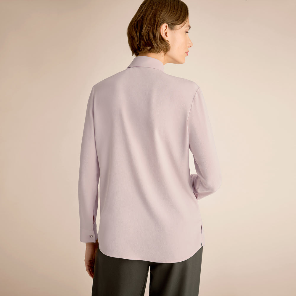 Person wearing a light purple shirt against a beige background