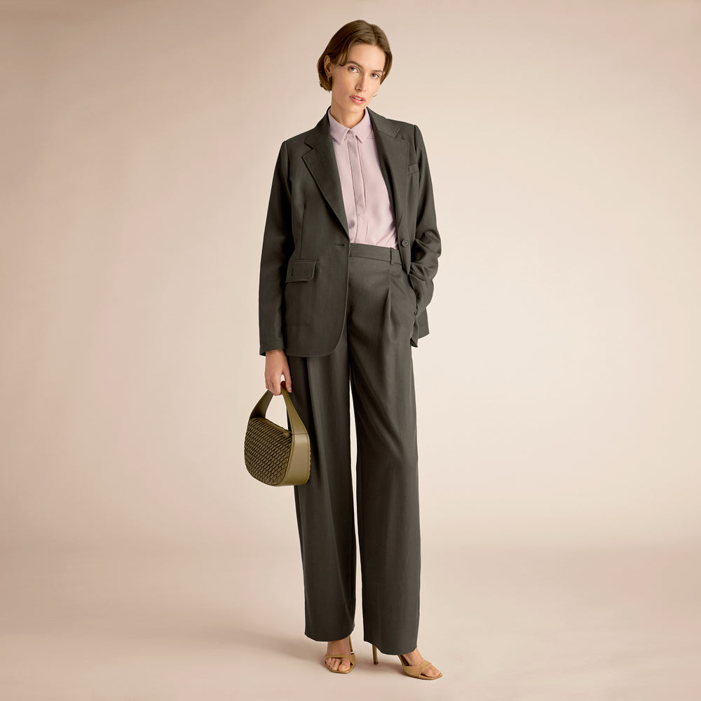 Woman in a gray suit holding a green handbag against a beige background