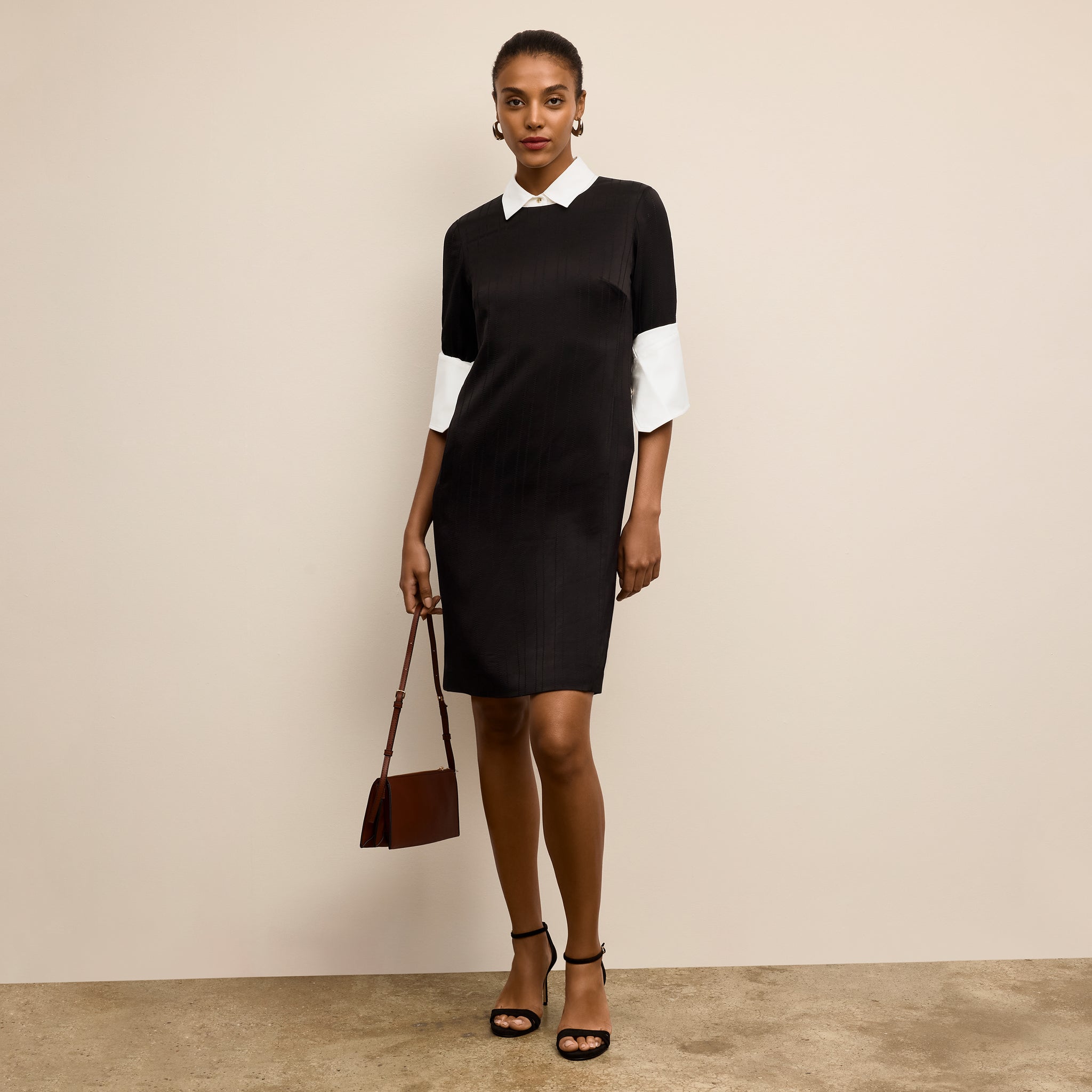Woman wearing a black and white dress holding a brown handbag against a beige background