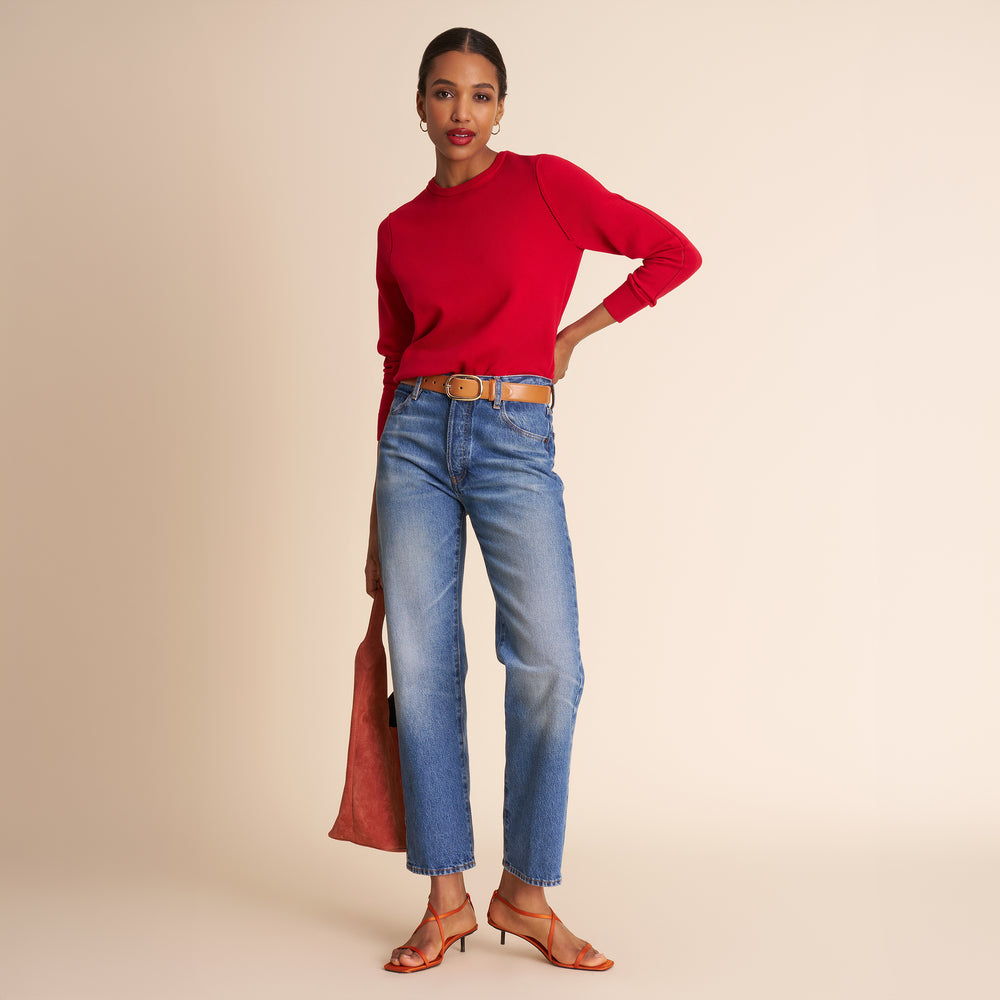 Woman wearing a red sweater and blue jeans on a beige background