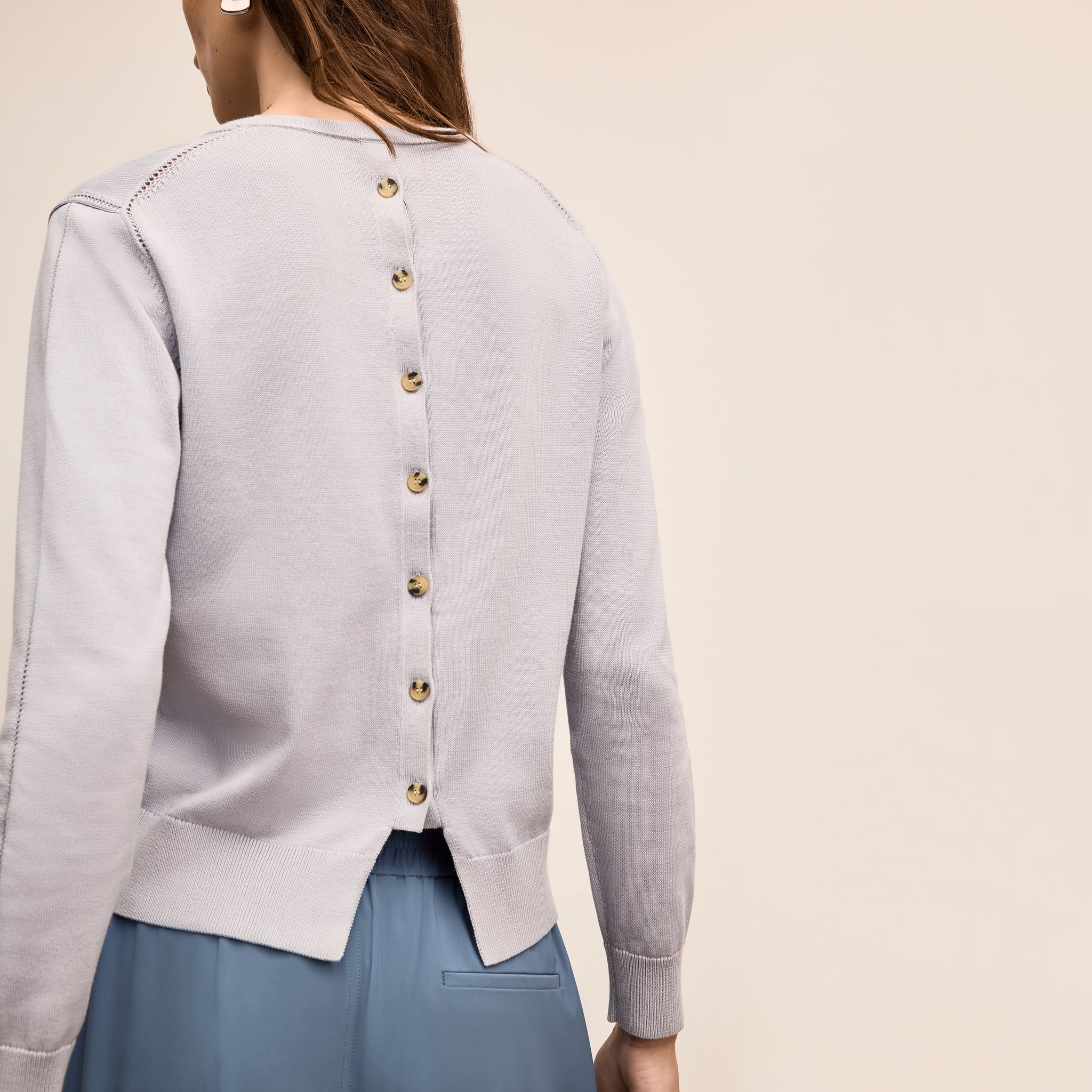 Light gray cardigan with gold buttons worn by a person on a beige background