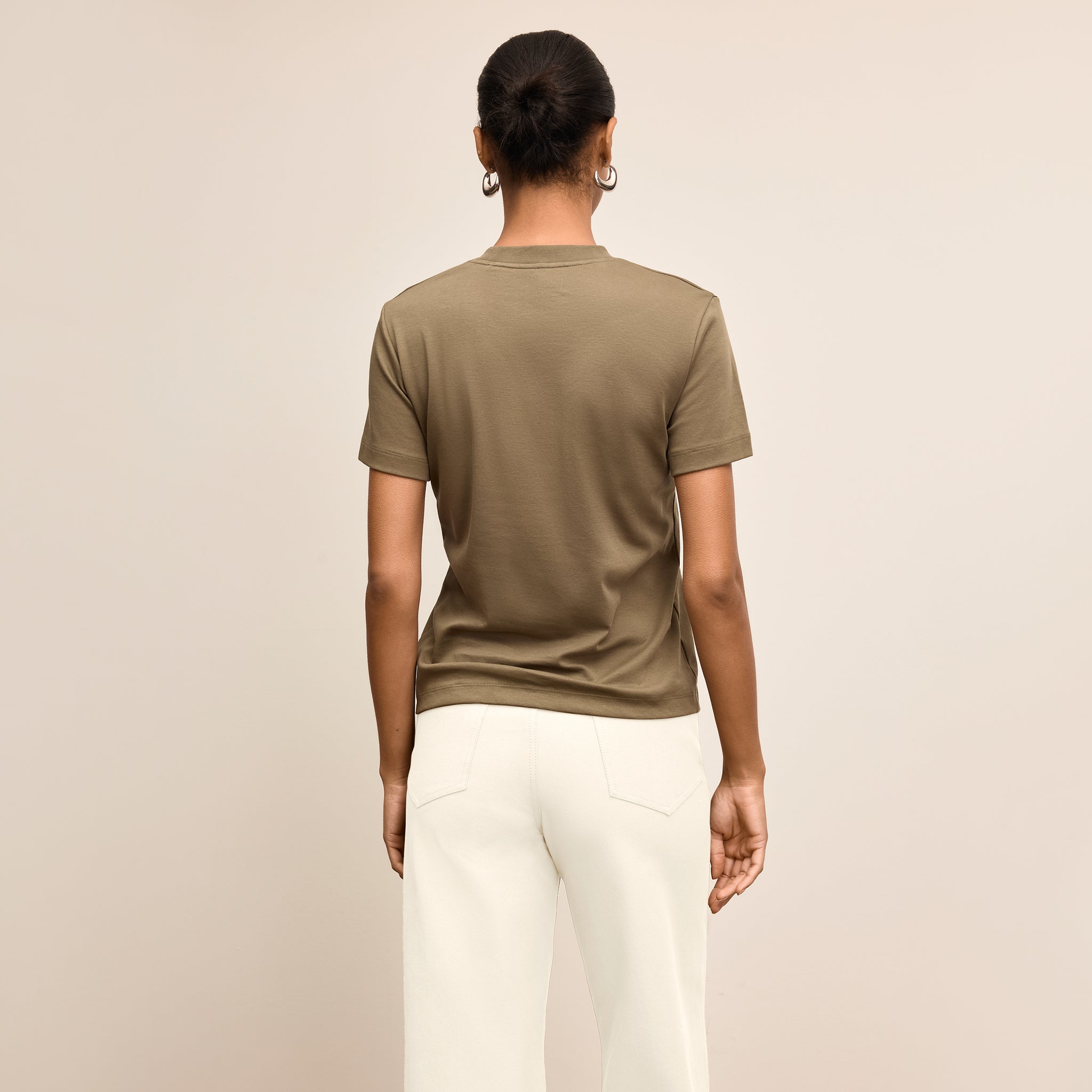 Person wearing a brown t-shirt and white pants on a beige background