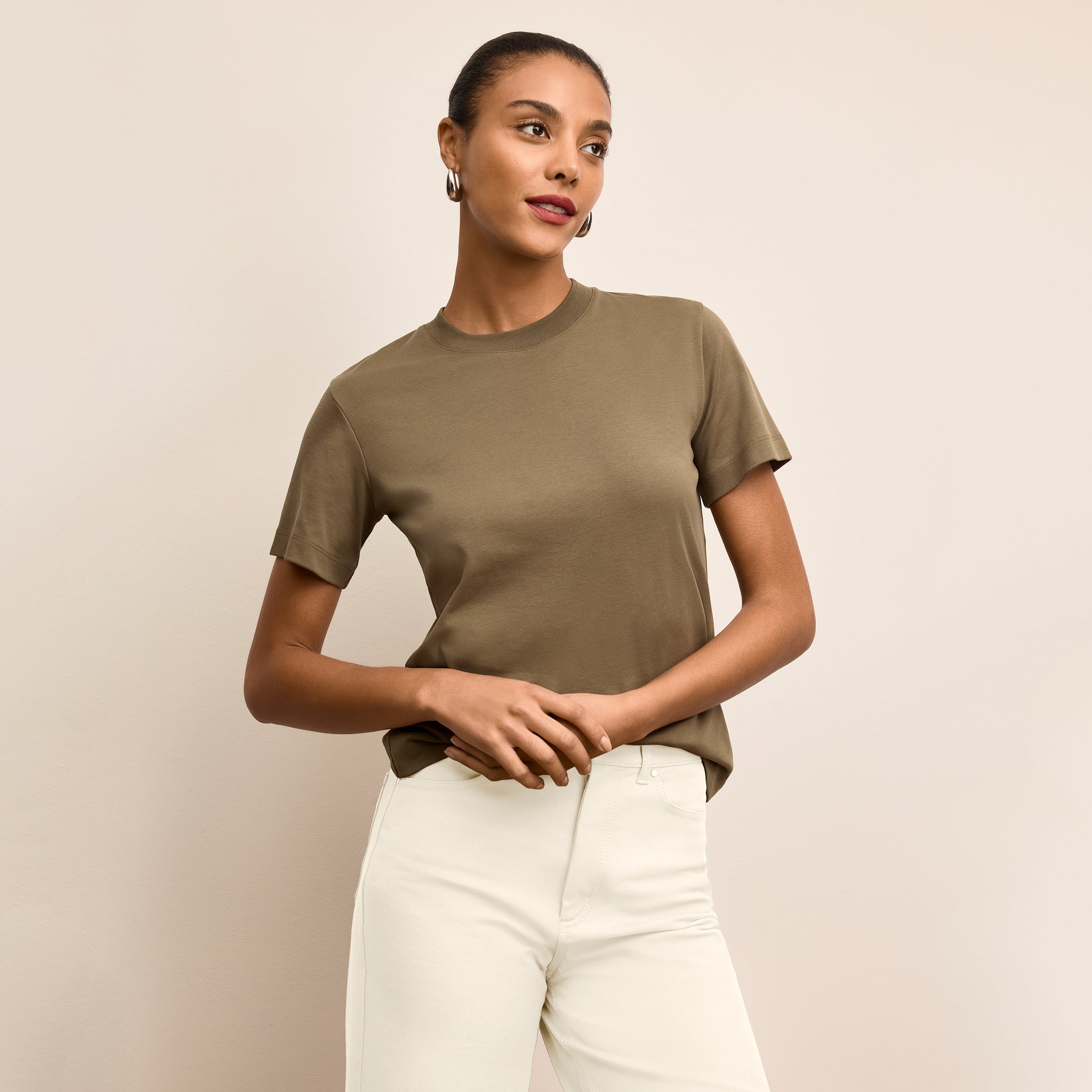 Woman wearing a green t-shirt and white pants against a beige background 