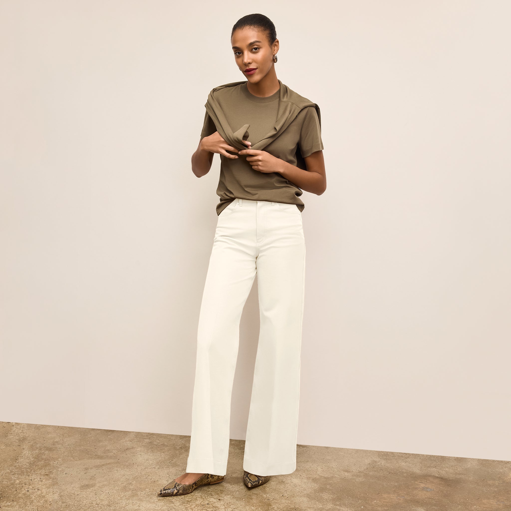 Woman wearing a green top and white pants against a plain background