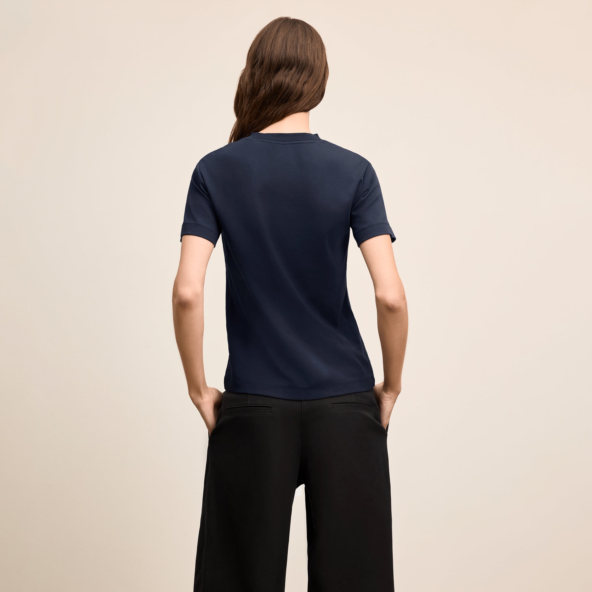 Person wearing a navy blue t-shirt and black pants on a beige background