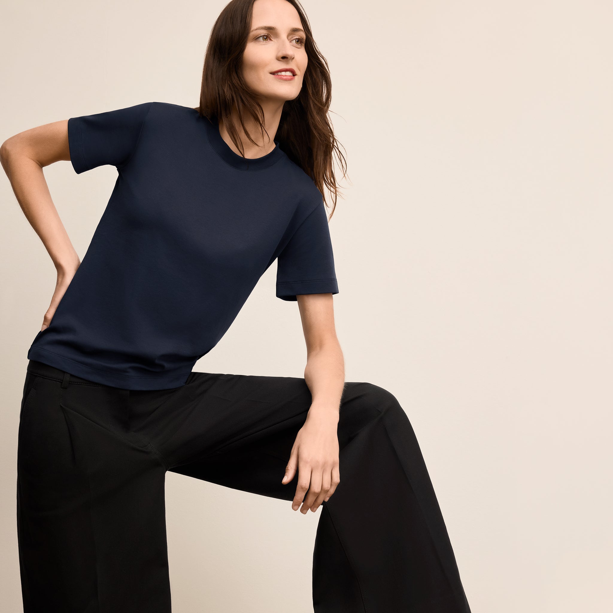 Woman wearing a navy blue top and black pants against a beige background 