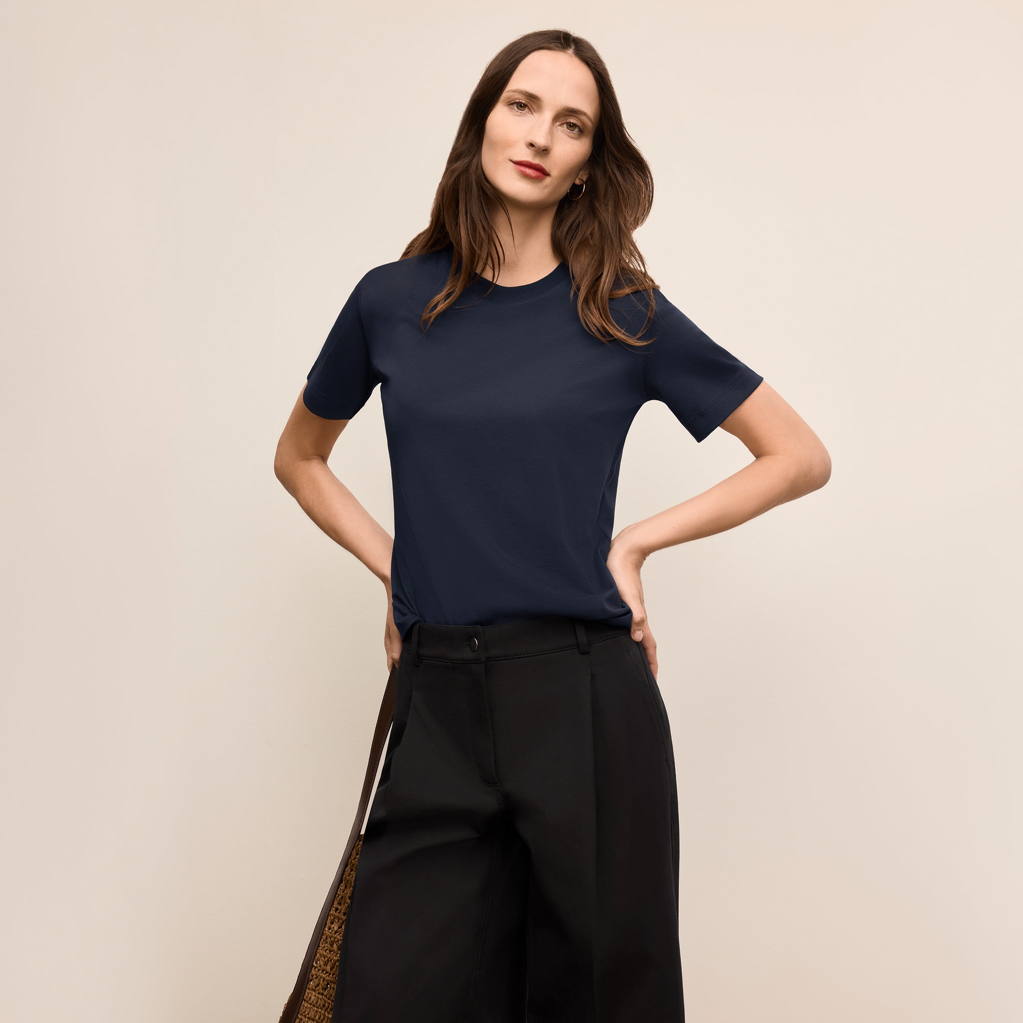 Woman wearing a navy blue t-shirt and black pants against a beige background