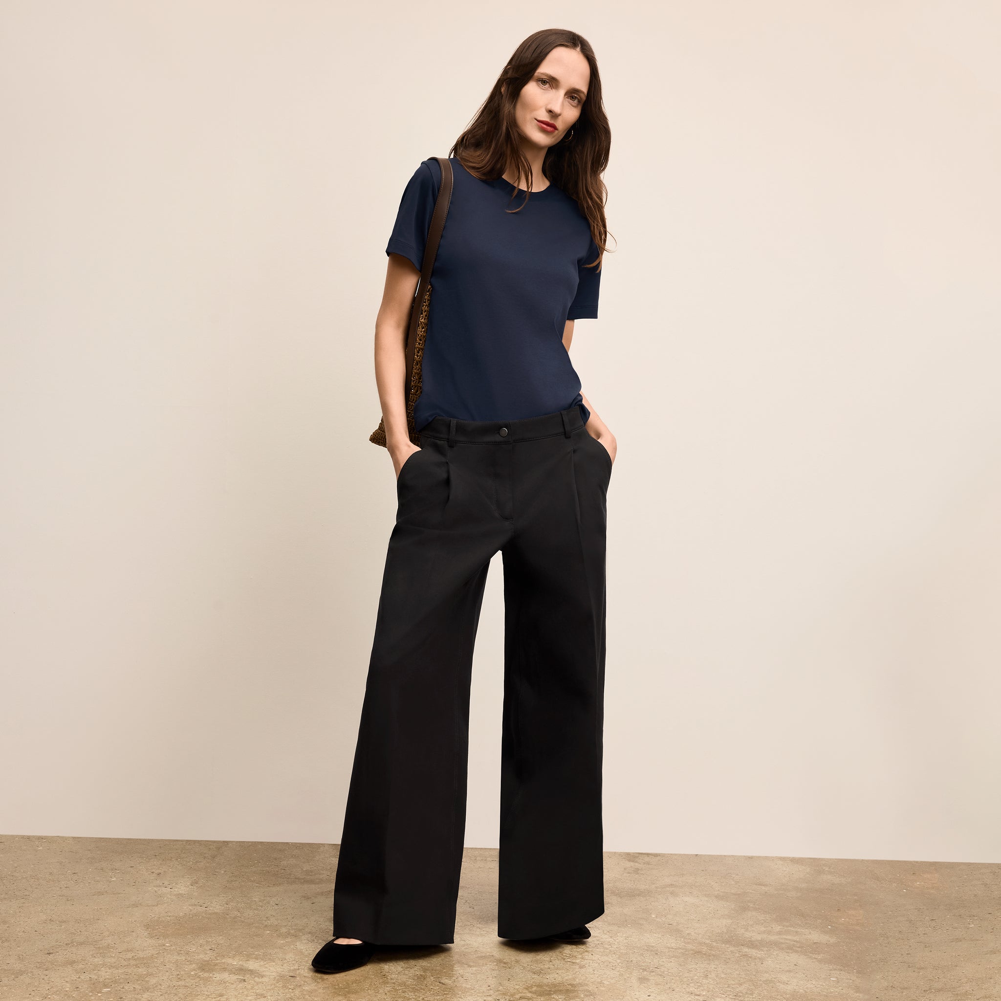 Woman wearing a navy blue top and black wide-leg pants against a beige background