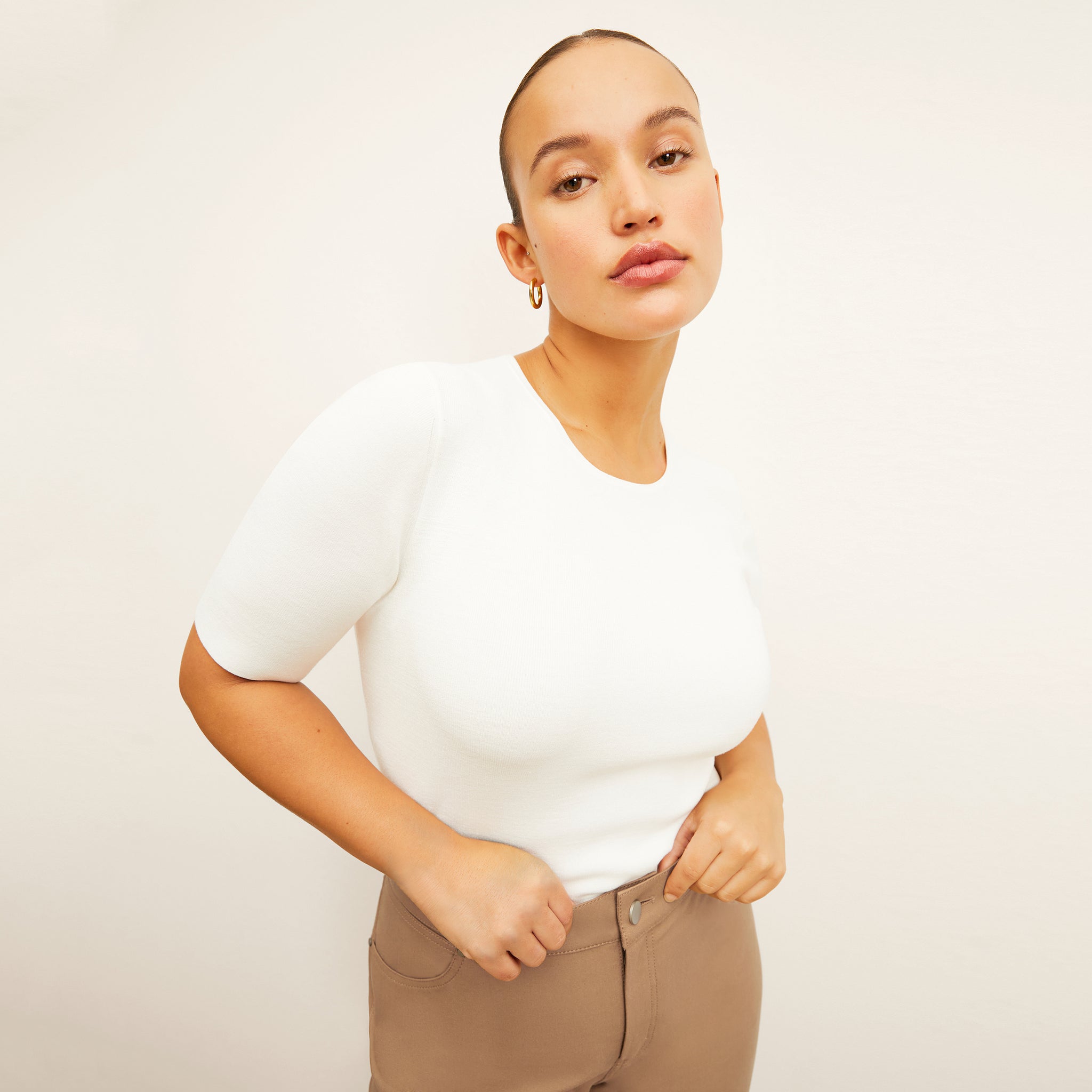 Side image of a woman standing wearing the choe top in ivory 