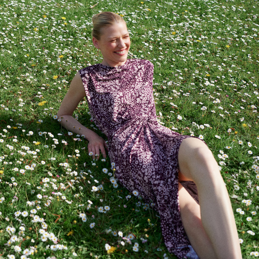 Woman in a purple dress sitting on a grassy field with flowers