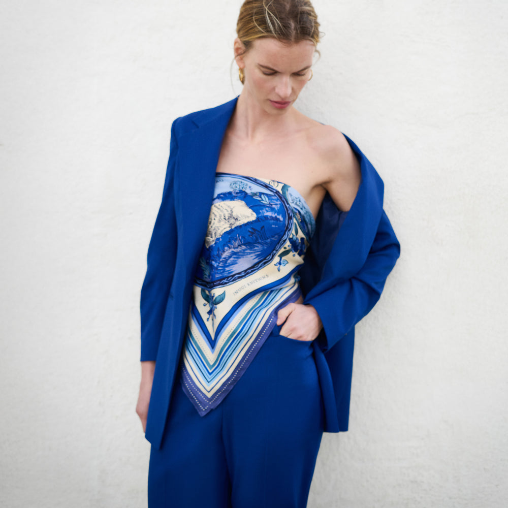 Woman wearing a blue outfit with a patterned scarf against a white background