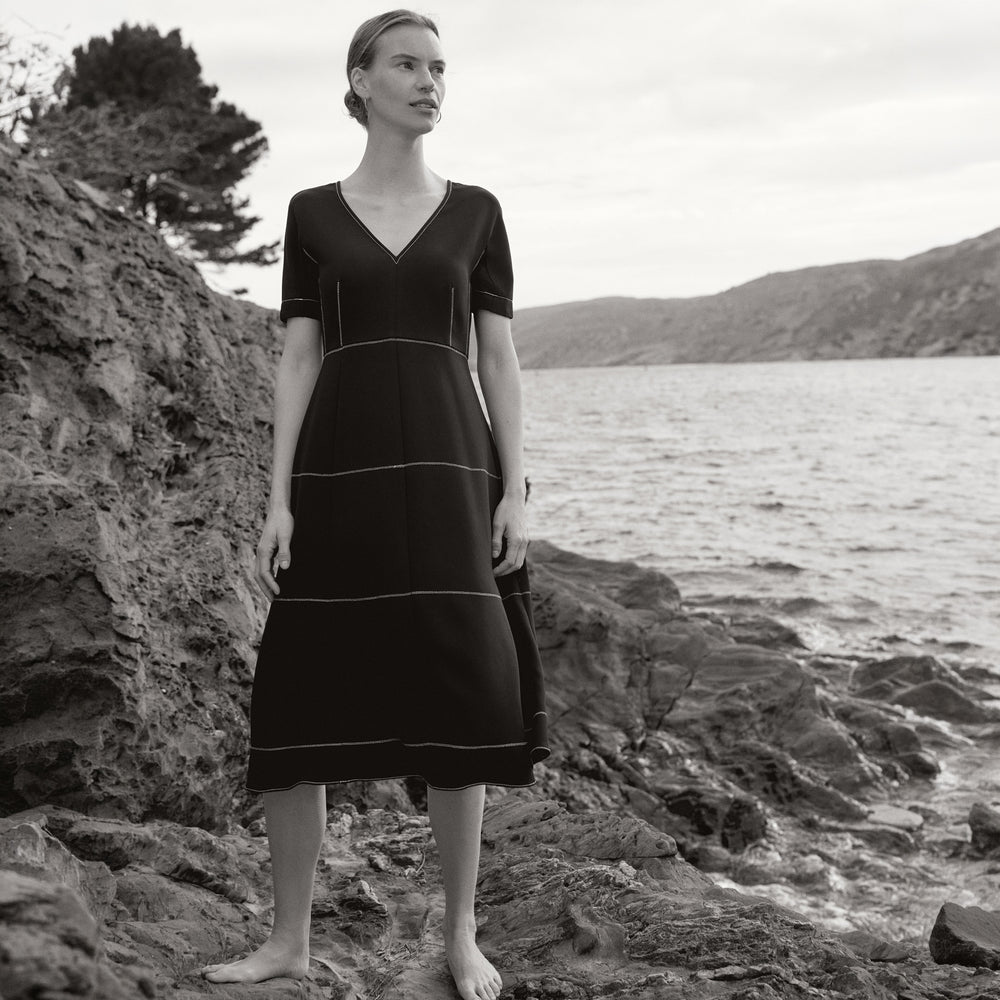 Woman in a black dress standing on a rocky beach with mountains in the background
