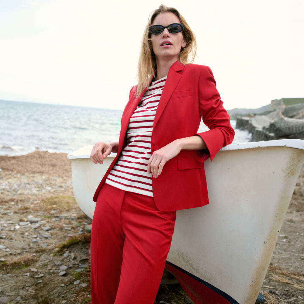 Woman in a red suit and striped shirt standing by a boat on a beach.